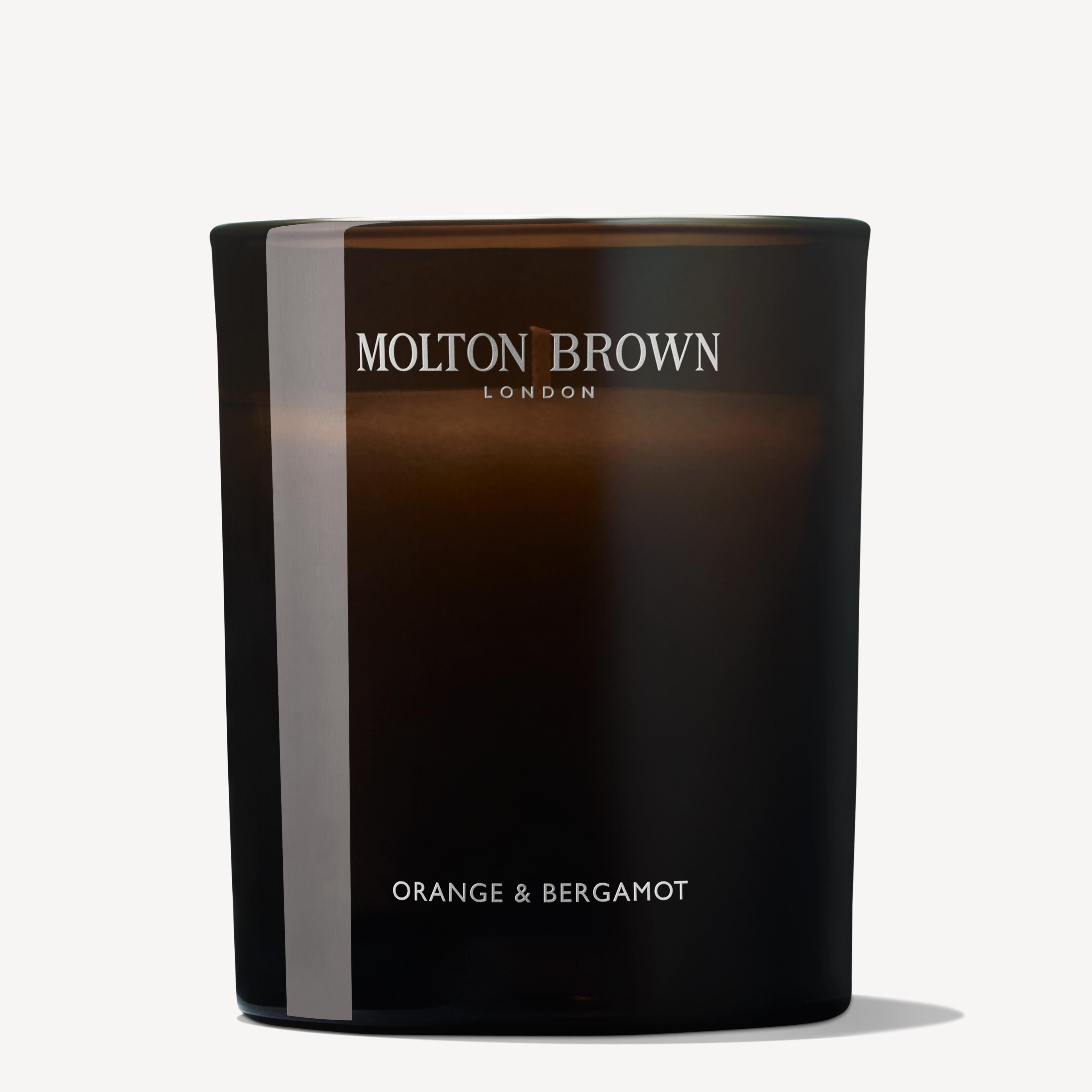A donkere glazen Orange & Bergamot Signature Kaars 190g van MoltonBrown Nederlands met een enkele lont straalt een energieke gloed uit tegen een witte achtergrond.