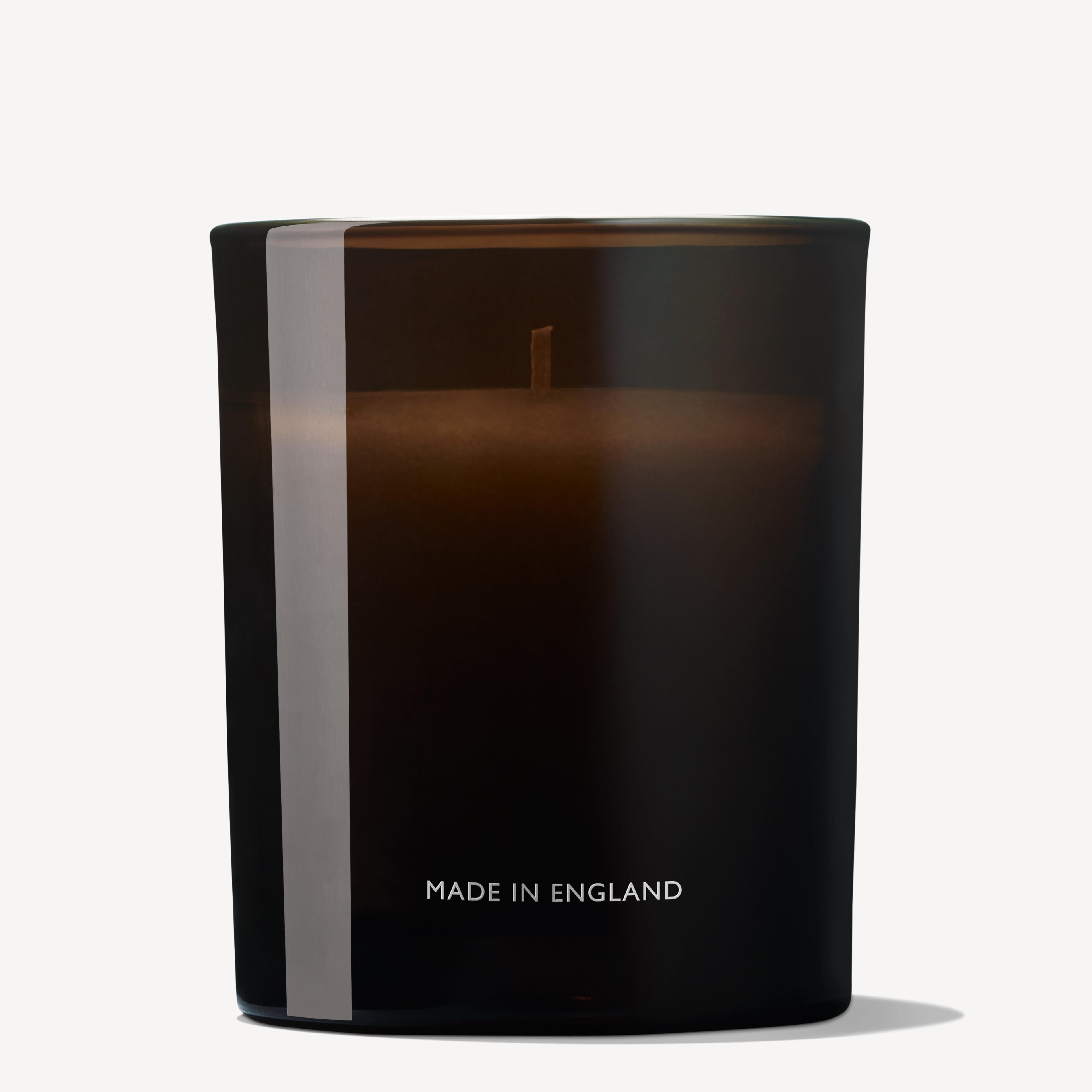 The MoltonBrown Nederlands Orange & Bergamot Signature Kaars 190g is a dark brown glass geurkaars met één lont en MADE IN ENGLAND op de voorkant, die een energieke gloed uitstraalt tegen een witte achtergrond.