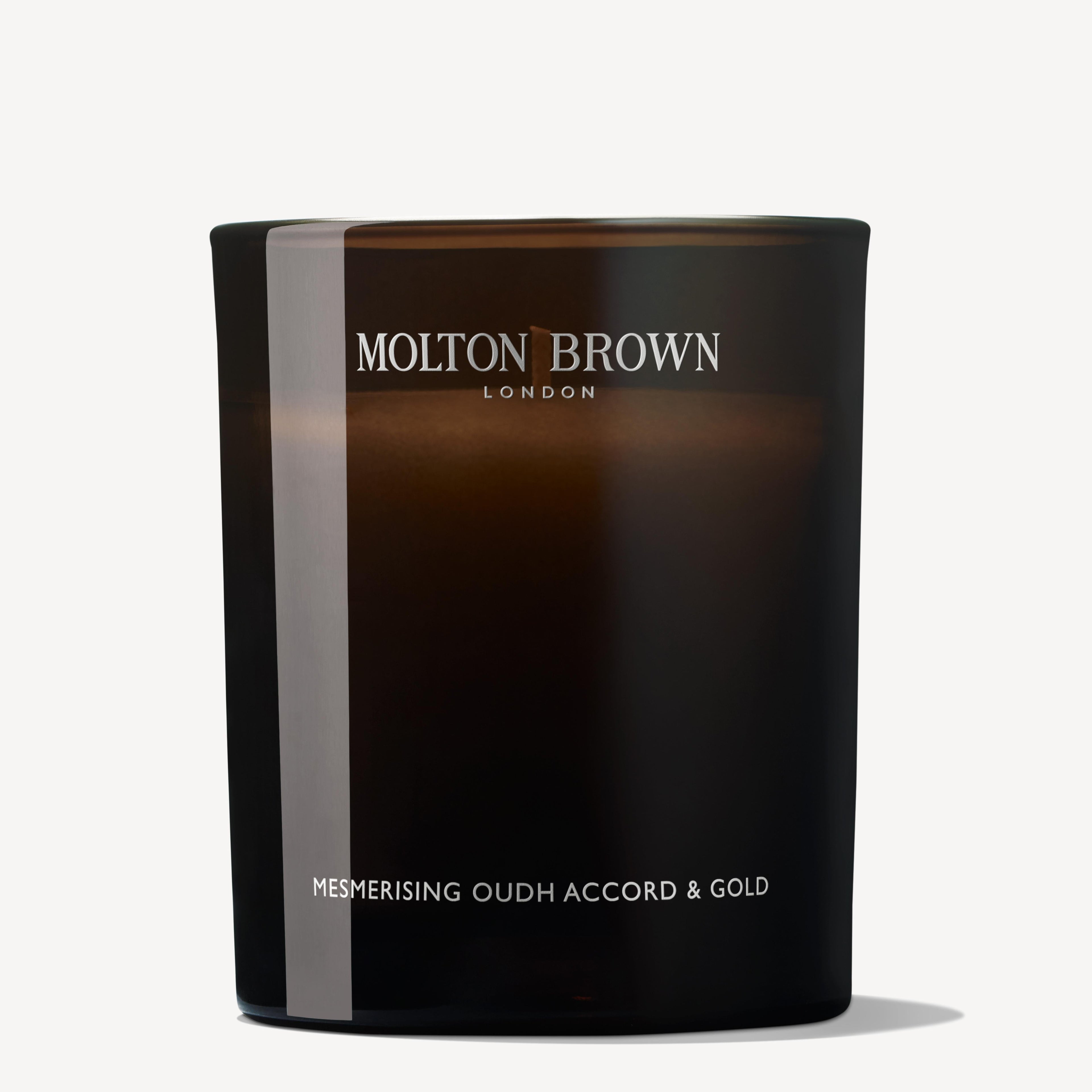 A modern, minimalist dark brown glass geurkaars with 'MoltonBrown Nederlands' and 'Mesmerising Oudh Accord & Gold Signature Kaars 190g' in white on the front; the candle is unlit.