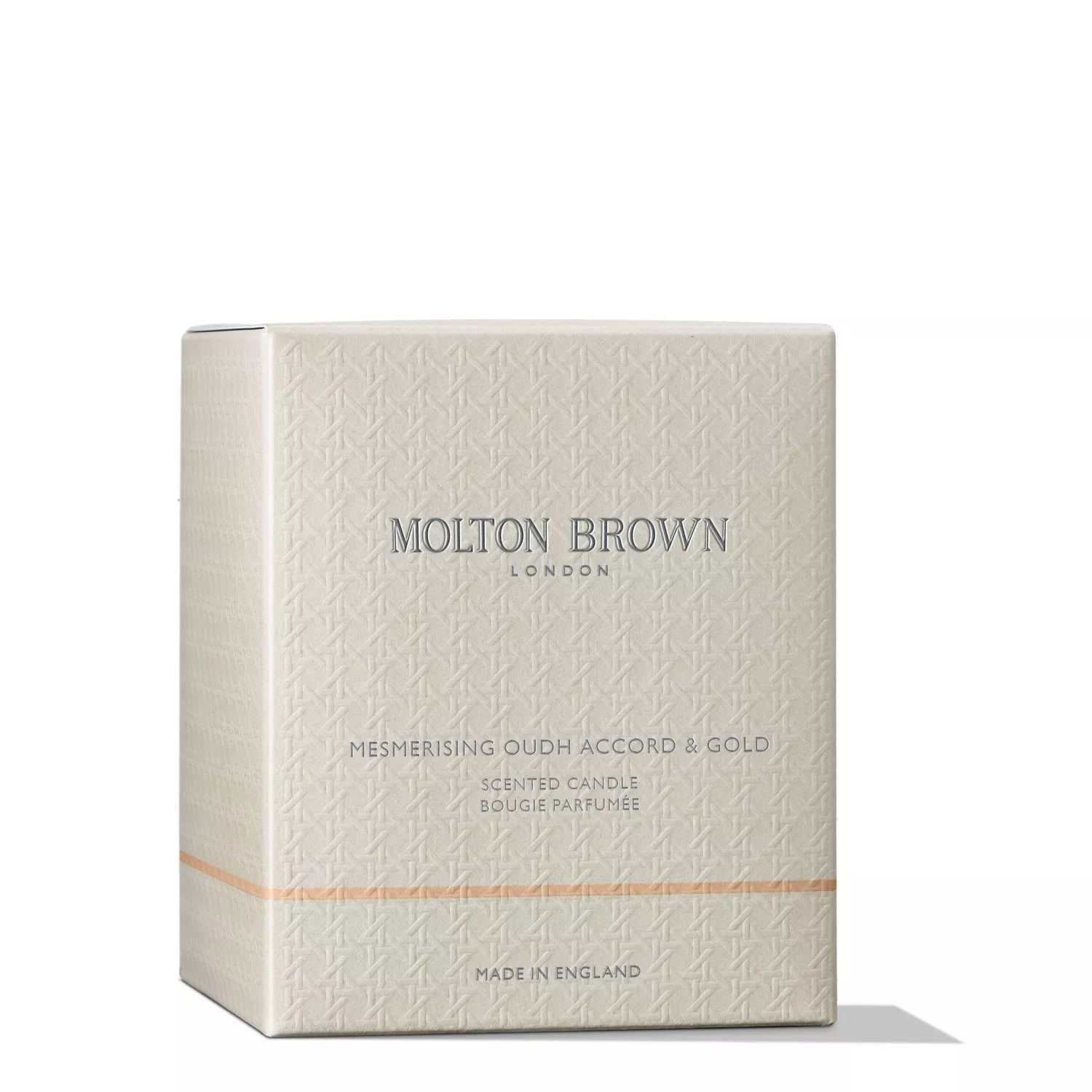 A beige box of MoltonBrown Nederlands Mesmerising Oudh Accord & Gold Luxury Kaars 600g, with subtle patterns, silver letters, and a slim gold stripe for an oosterse sfeer.