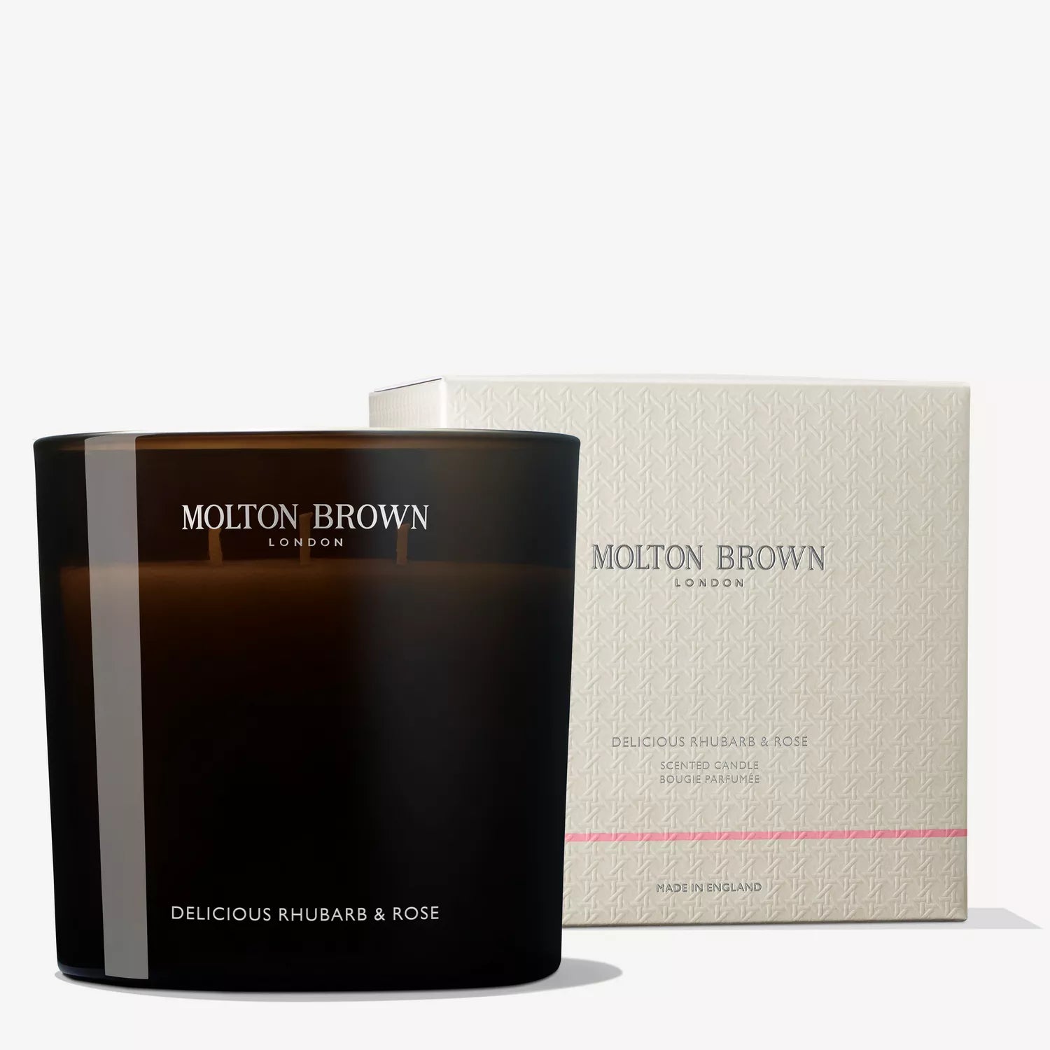 A MoltonBrown Nederlands Delicious Rhubarb & Rose Luxury Kaars 600g sits before a branded light box. The packaging has subtle patterns, a pink stripe, and hints at its bloemig-fruitige fragrance.
