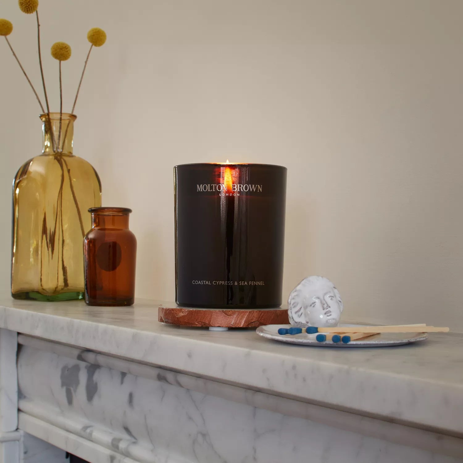 The MoltonBrown Nederlands Coastal Cypress & Sea Fennel Signature Kaars 190g sits on a marble shelf, gently filling the room with refined coastal aromas.