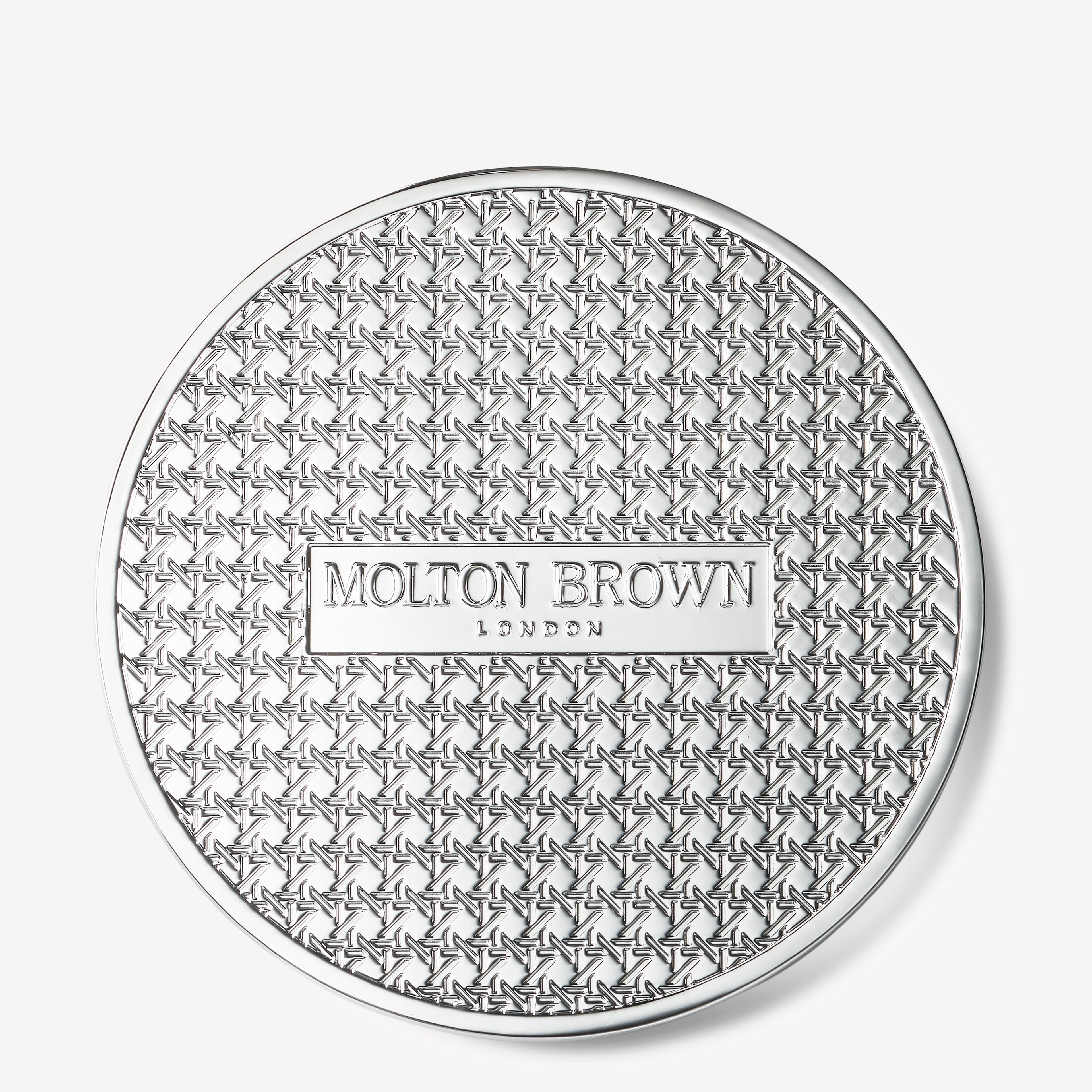 A round, silver-toned Luxury Kaars Lid 154g by MoltonBrown Nederlands features a geometric star pattern and a raised rectangular label in the center that reads Molton Brown London.