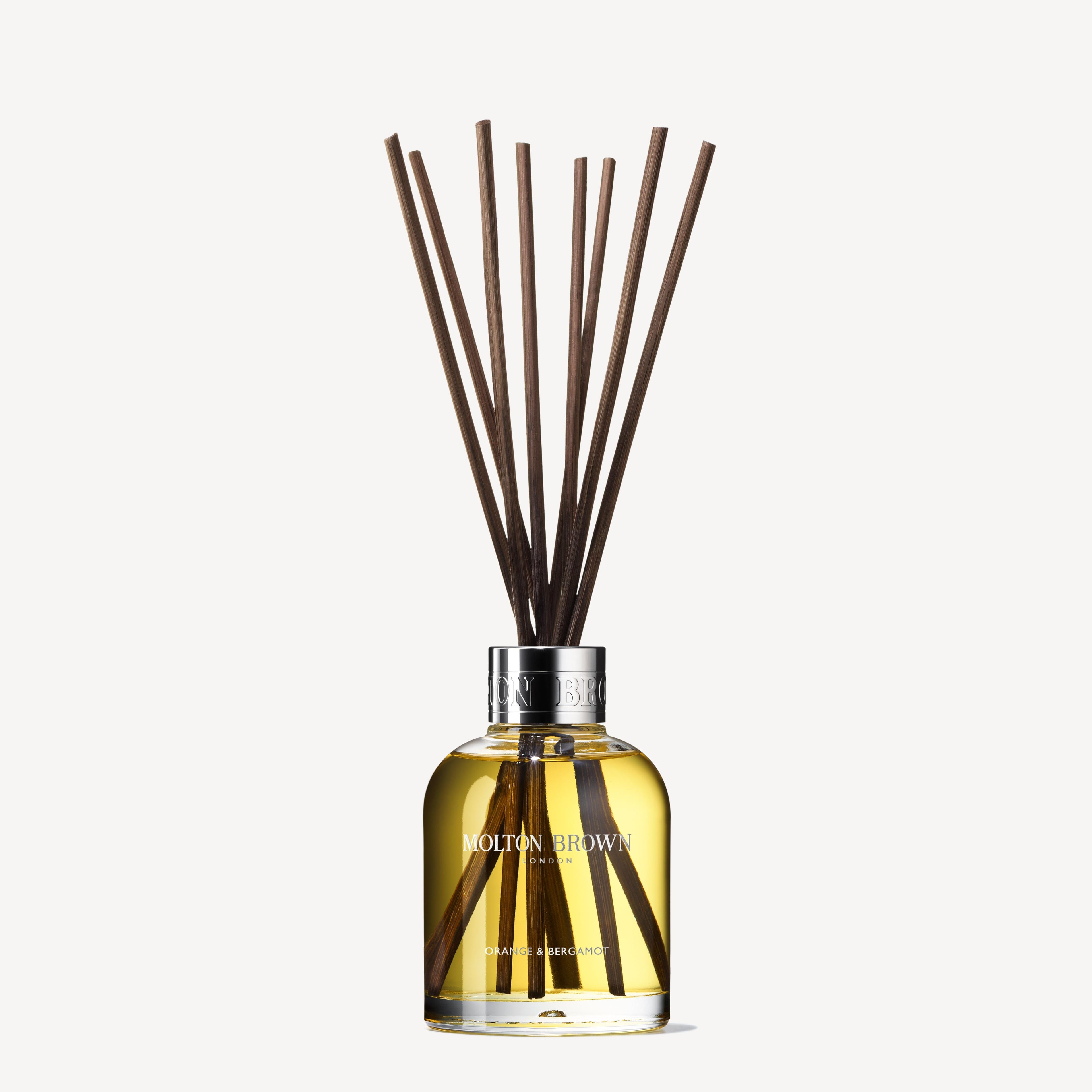 A clear MoltonBrown Nederlands bottle, labeled "test 2 Orange & Bergamot Geurstokjes 150ml (Copy)," has a silver cap and geurstokjes. It releases an uplifting citrus scent inspired by orange and bergamot.