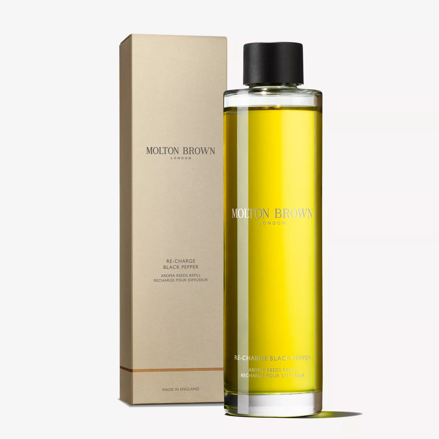 A clear bottle of MoltonBrown Nederlands Re-charge Black Pepper Geurstokjes Navulling 150ml with yellow liquid stands next to its beige box, both with minimalist branding, highlighting its houtig-citrus geur.