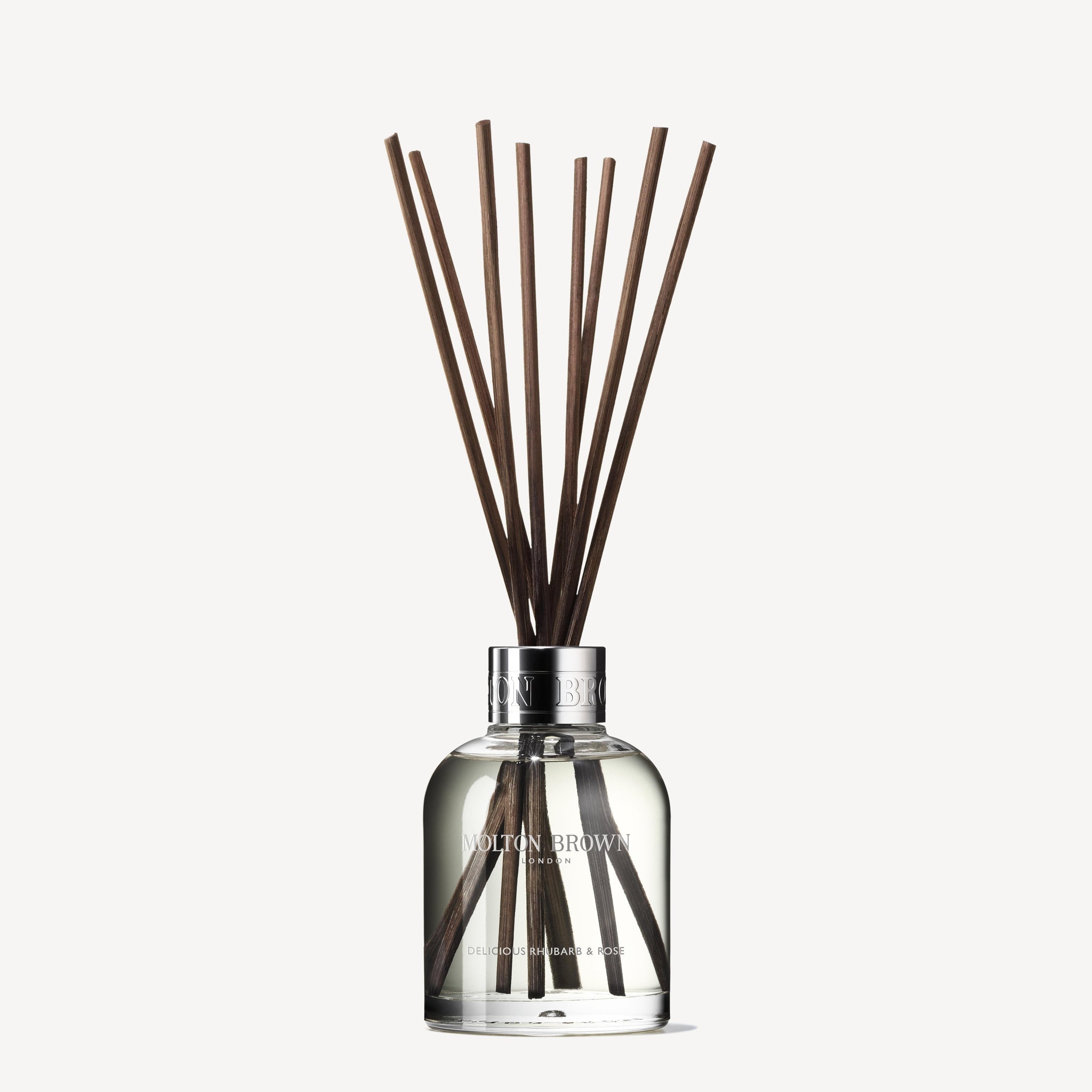 The MoltonBrown Nederlands test 3 Delicious Rhubarb & Rose Geurstokjes 150ml (Copy) diffuser features a clear bottle and brown sticks, adding a bloemig-fruitige geur to your interieur. Displayed against a white background.