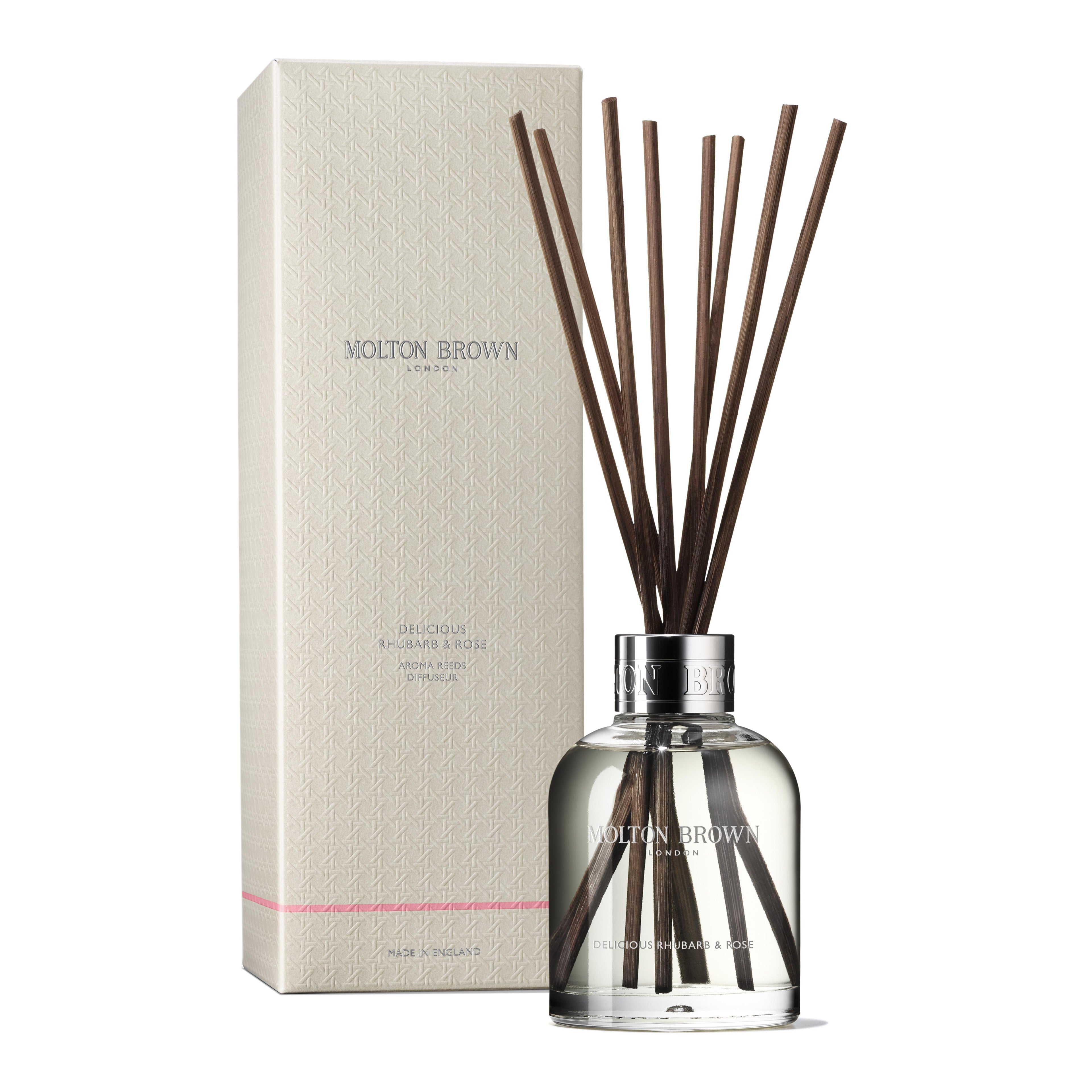 The MoltonBrown Nederlands test 3 Delicious Rhubarb & Rose Geurstokjes 150ml comes in a clear glass bottle with brown reeds beside its cream box, bringing a bloemig-fruitige geur to your interieur. The label shows Delicious Rhubarb & Rose.