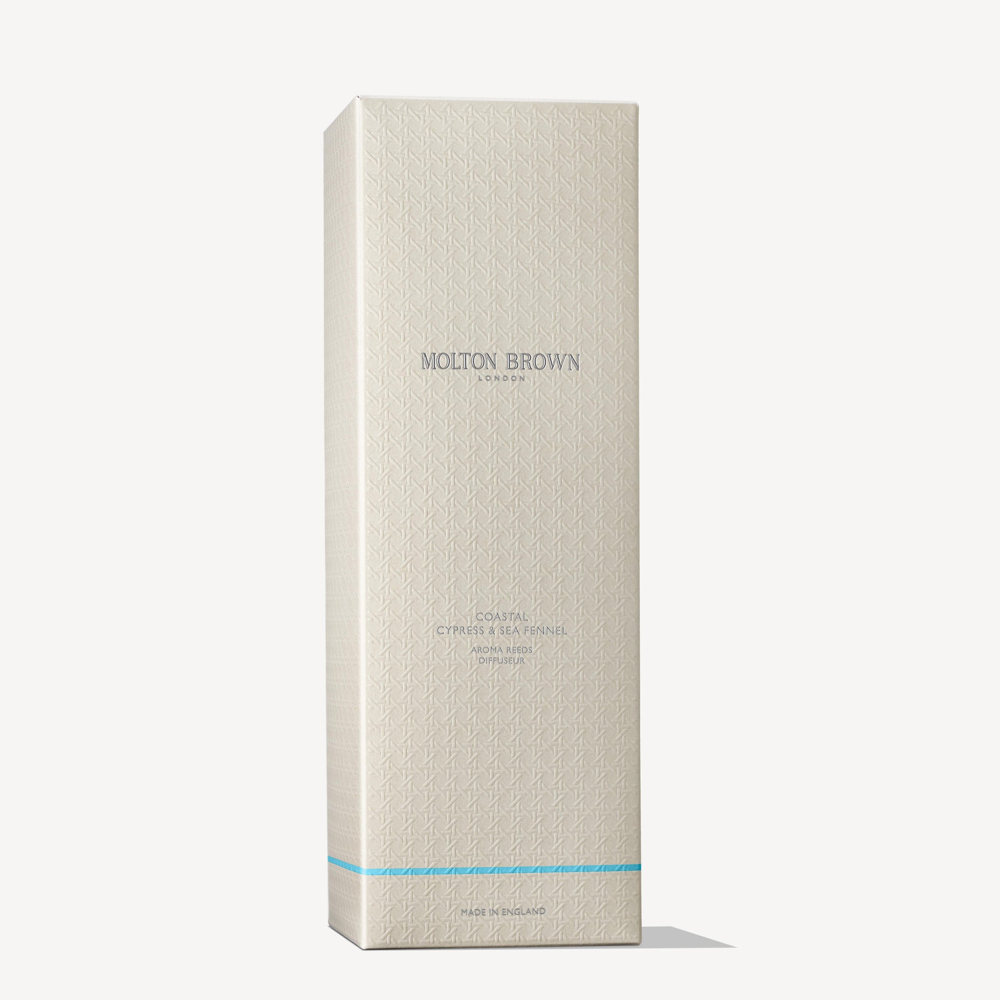 A tall, rectangular cream-colored MoltonBrown Nederlands box with subtle geometric patterns and light blue "Coastal Cypress & Sea Fennel Geurstokjes 150ml" text stands upright against a white background—ideal for housing luxe geurstokjes.