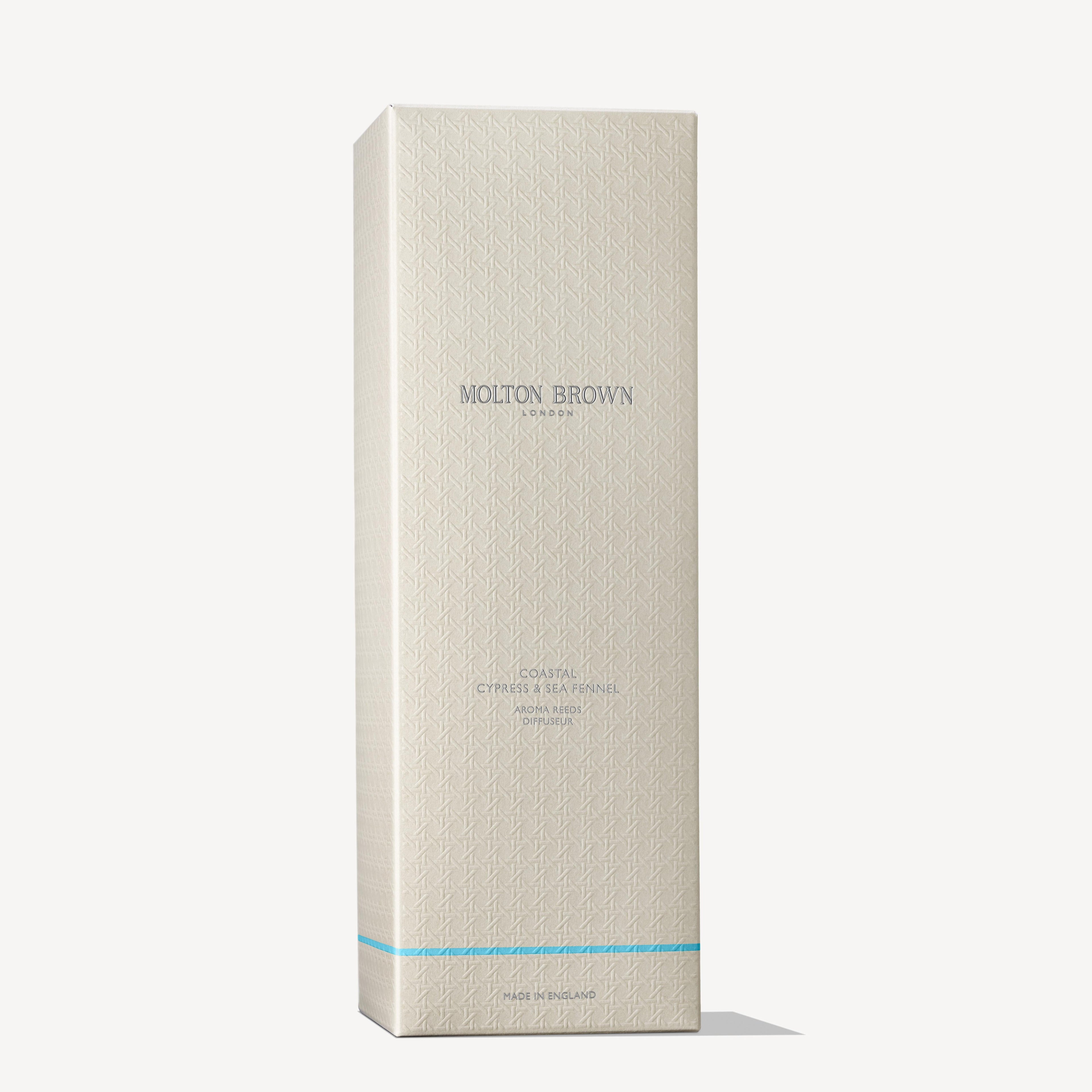 A tall, rectangular cream-colored MoltonBrown Nederlands box with subtle geometric patterns and light blue "Coastal Cypress & Sea Fennel Geurstokjes 150ml" text stands upright against a white background—ideal for housing luxe geurstokjes.