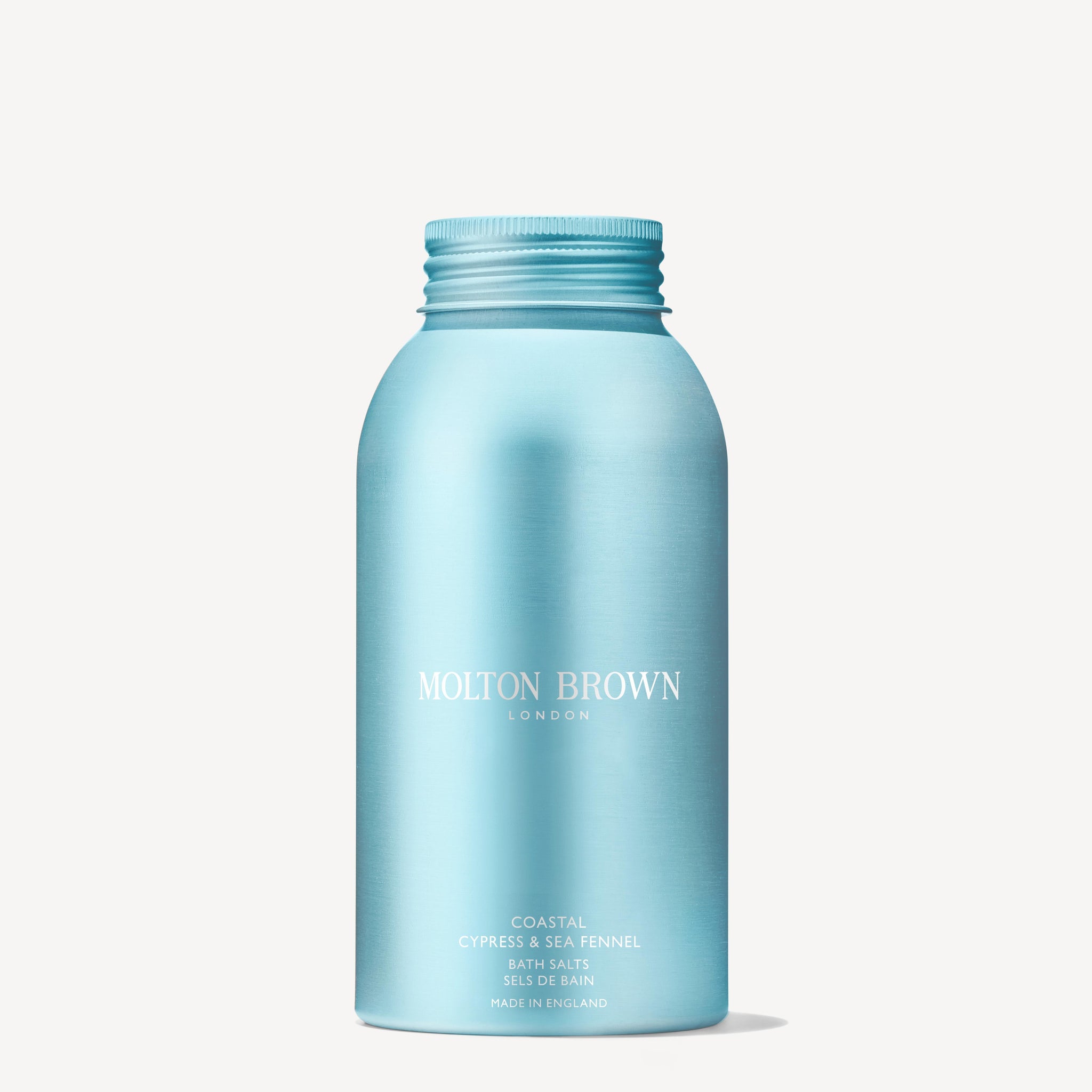 A metallic light blue 300g bottle of MoltonBrown Nederlands Coastal Cypress & Sea Fennel Badzout with a screw cap stands upright against a white background—ideal to pair with your favorite handzeep for a refreshing wash.