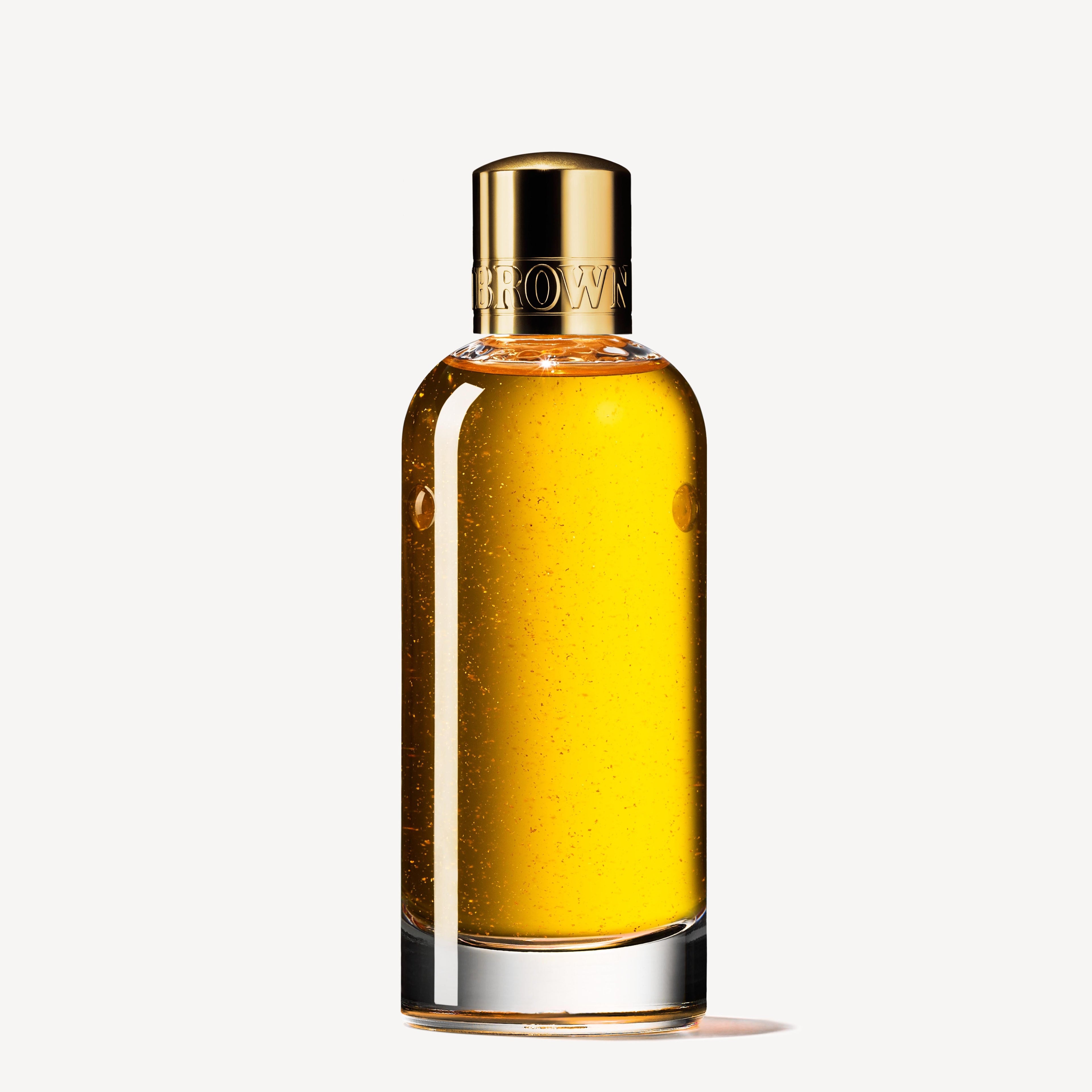 The MoltonBrown Nederlands Mesmerising Oudh Accord & Gold Precious Lichaamsolie 100ml is a clear glass bottle with golden yellow oil and a metallic gold embossed cap, shown upright against a plain white background.