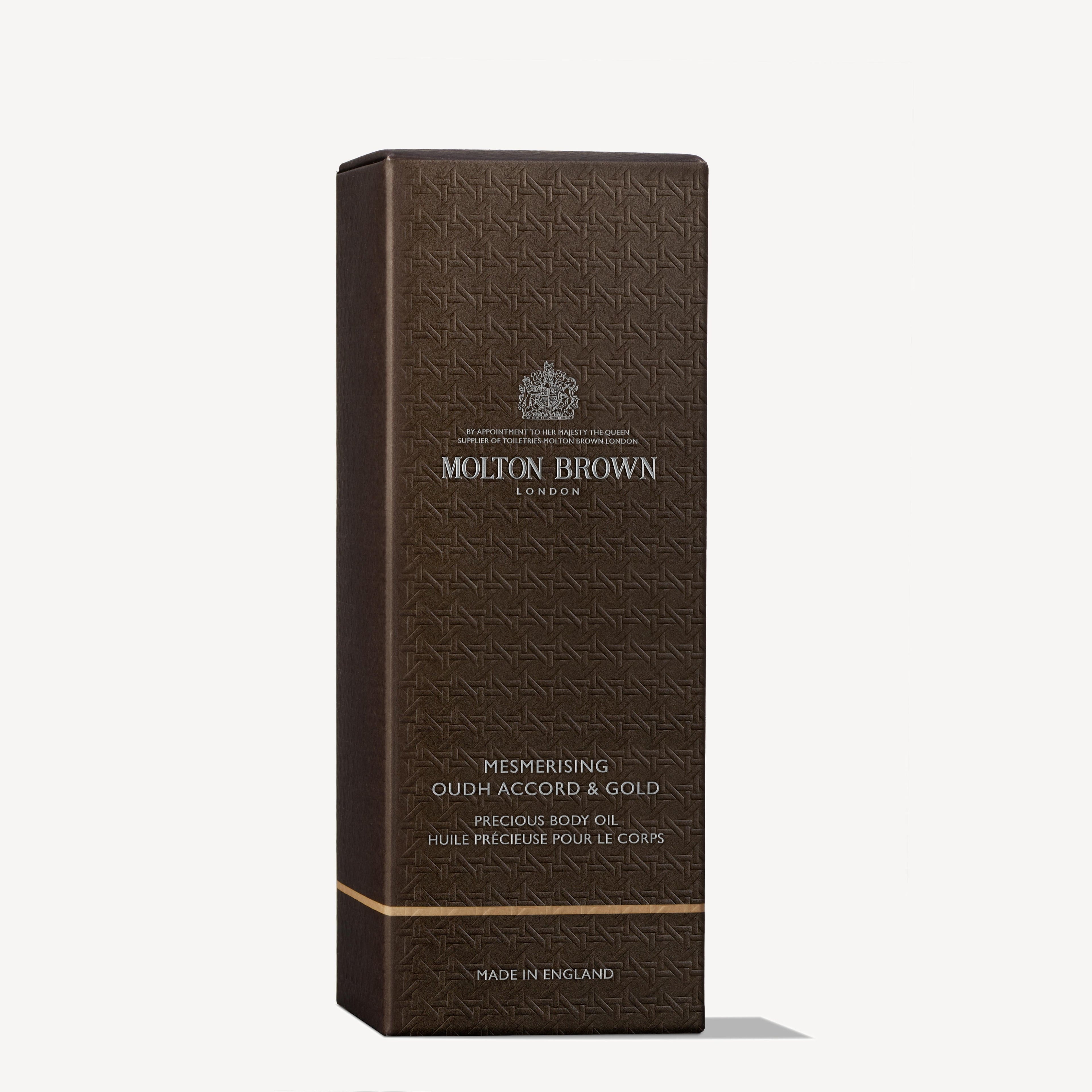 A rectangular, dark brown MoltonBrown Nederlands box labeled “Mesmerising Oudh Accord & Gold Precious Lichaamsolie 100ml” with a subtle pattern, silver text, and the Molton Brown London logo.