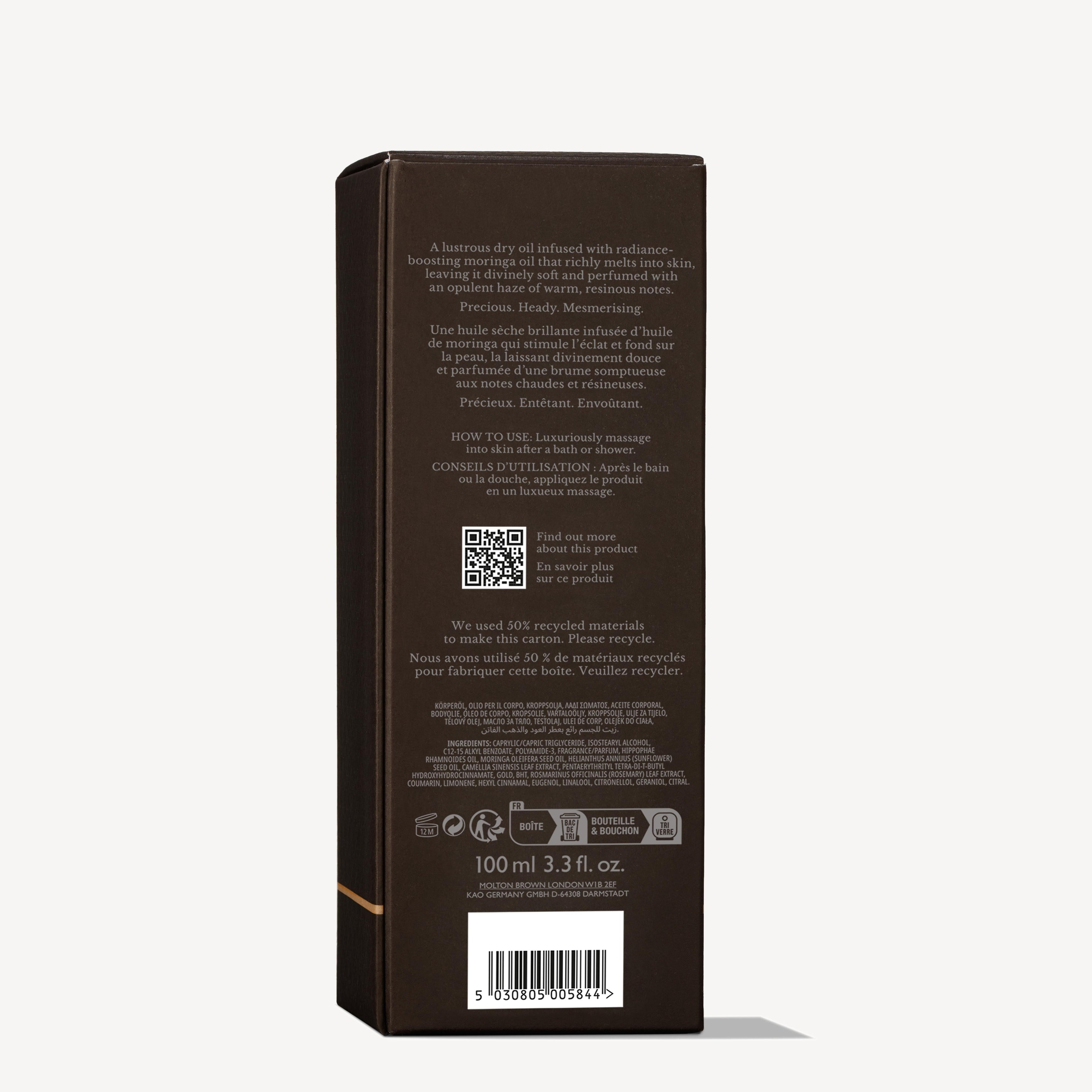A dark brown rectangular box of Mesmerising Oudh Accord & Gold Precious Lichaamsolie 100ml by MoltonBrown Nederlands stands upright. White text on the back shares product info, instructions, recycling details, and a barcode at the bottom.