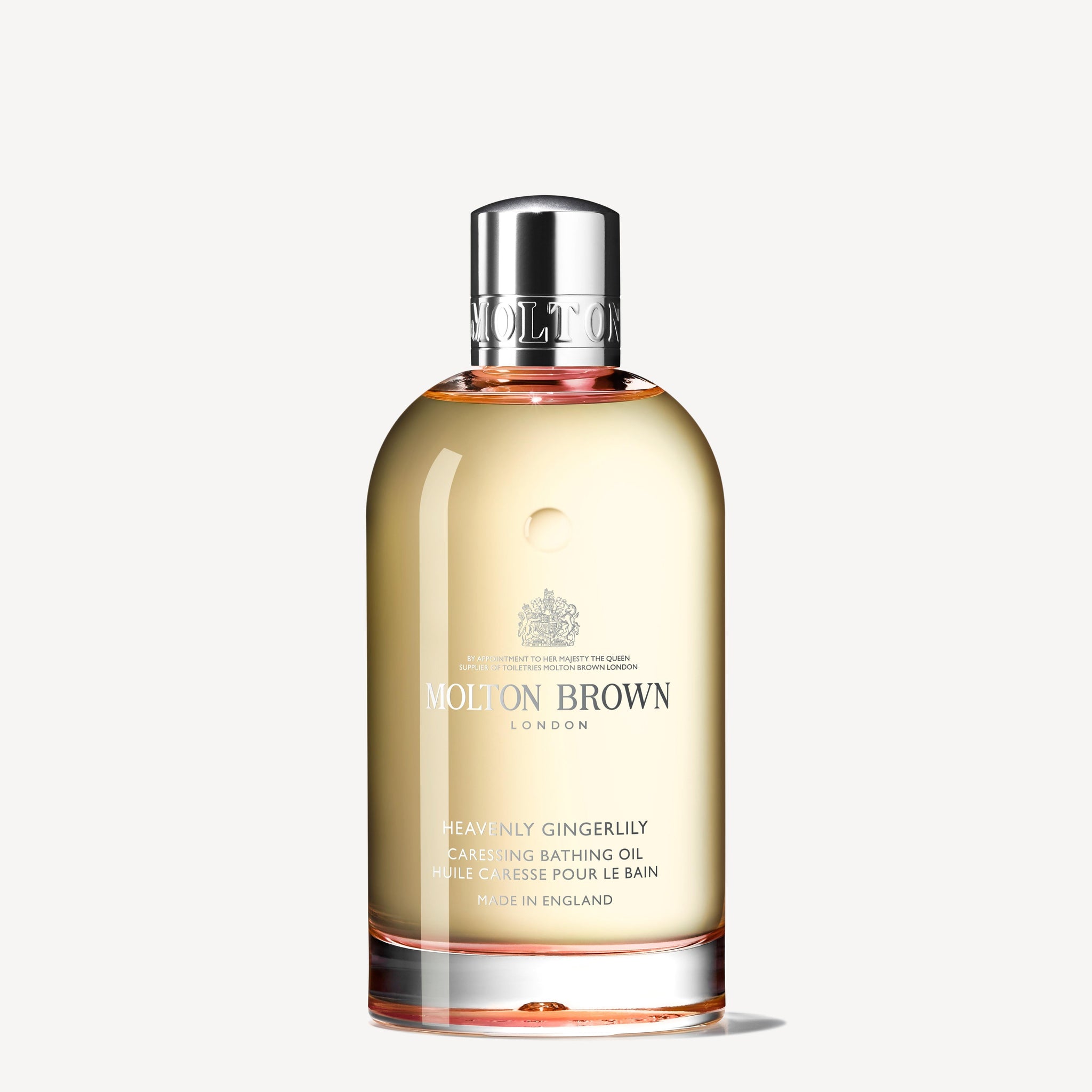 A clear bottle of MoltonBrown Nederlands Heavenly Gingerlily Caressing Bathing Oil 200ml with a silver cap, filled with light golden liquid, shown against a plain white background.