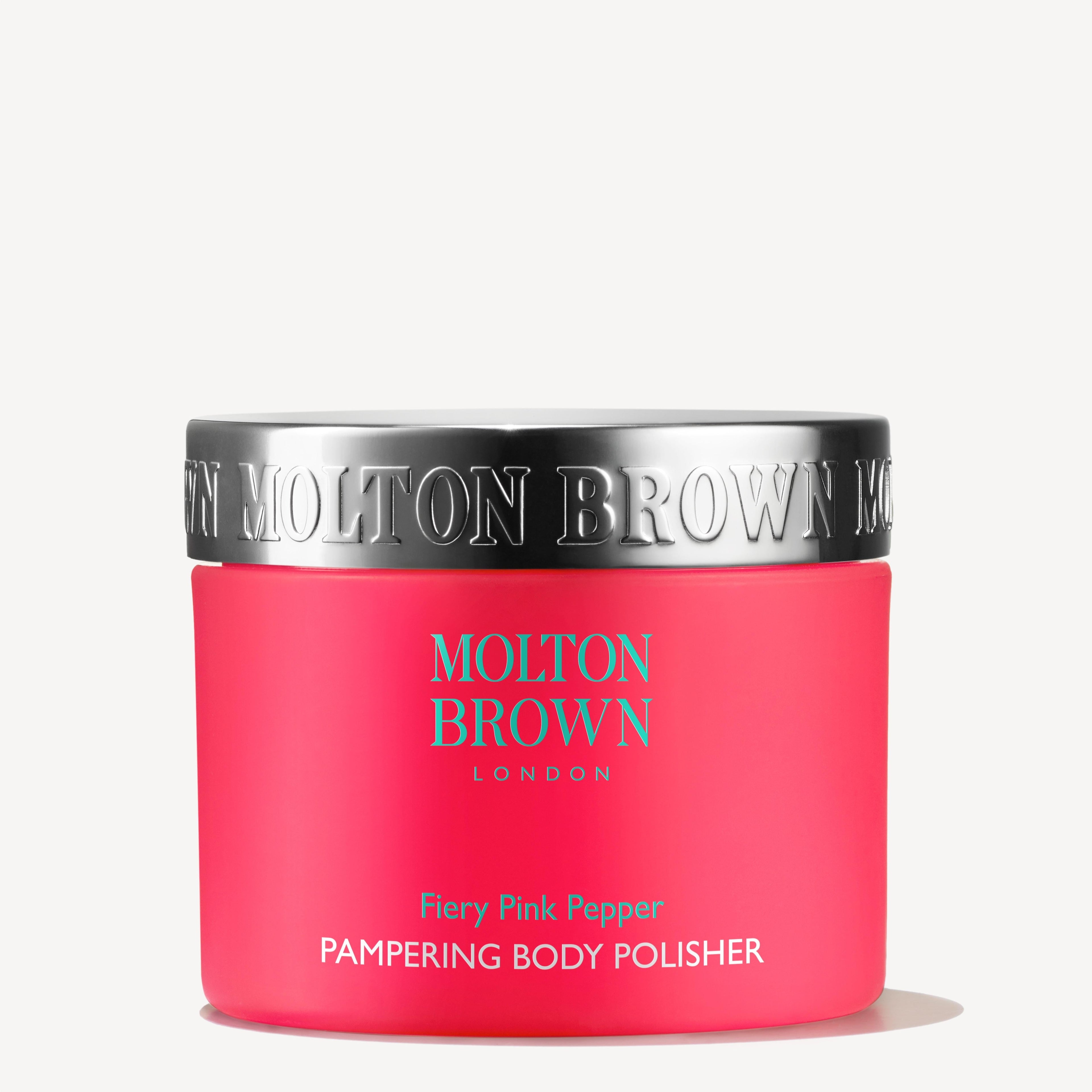A bright pink 275g jar of MoltonBrown Nederlands Fiery Pink Pepper Pampering Body Polisher, with exfoliërende jojoba korrels and a shiny silver lid, shown against a plain white background.