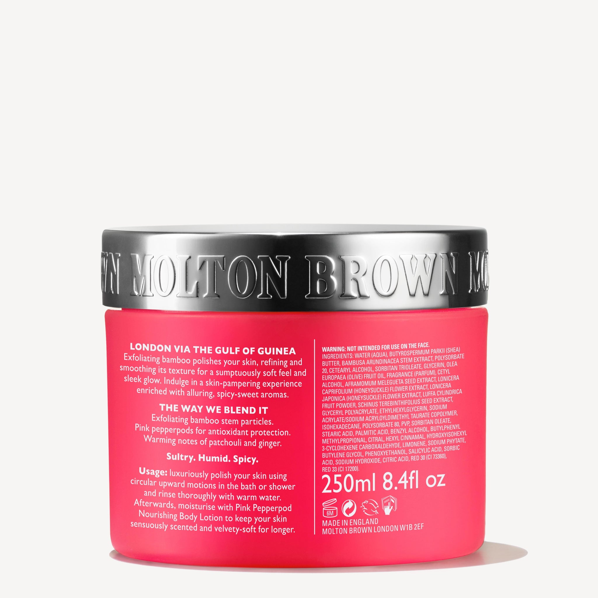 A vibrant pink jar of MoltonBrown Nederlands Fiery Pink Pepper Pampering Body Polisher (275g) with exfoliating jojoba beads and a metallic silver lid. The label lists origin, usage, ingredients, and volume.