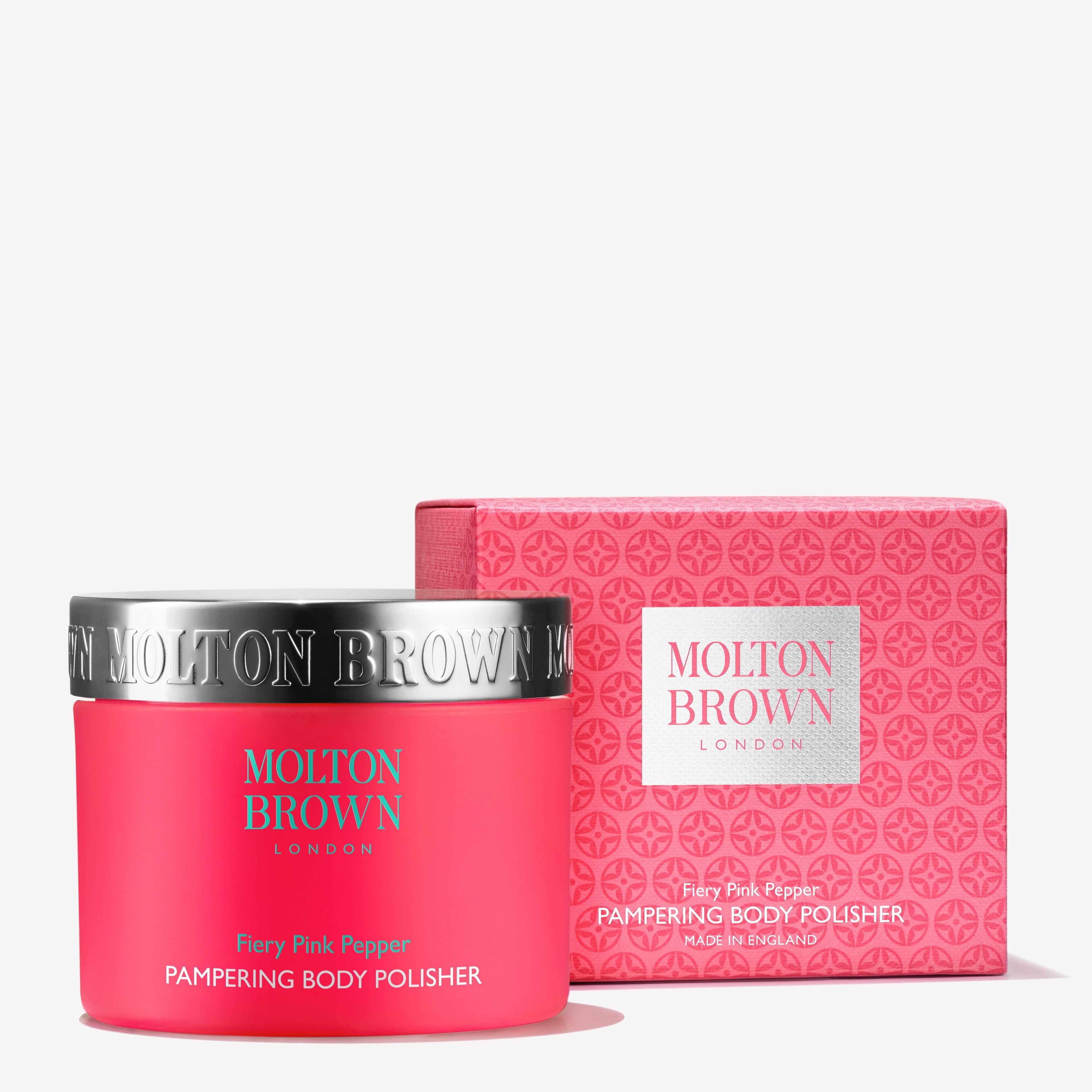 A pink jar and matching box of MoltonBrown Nederlands Fiery Pink Pepper Pampering Body Polisher 275g, featuring silver accents and bold text, with exfoliërende jojoba korrels for a luxurious touch on a white background.