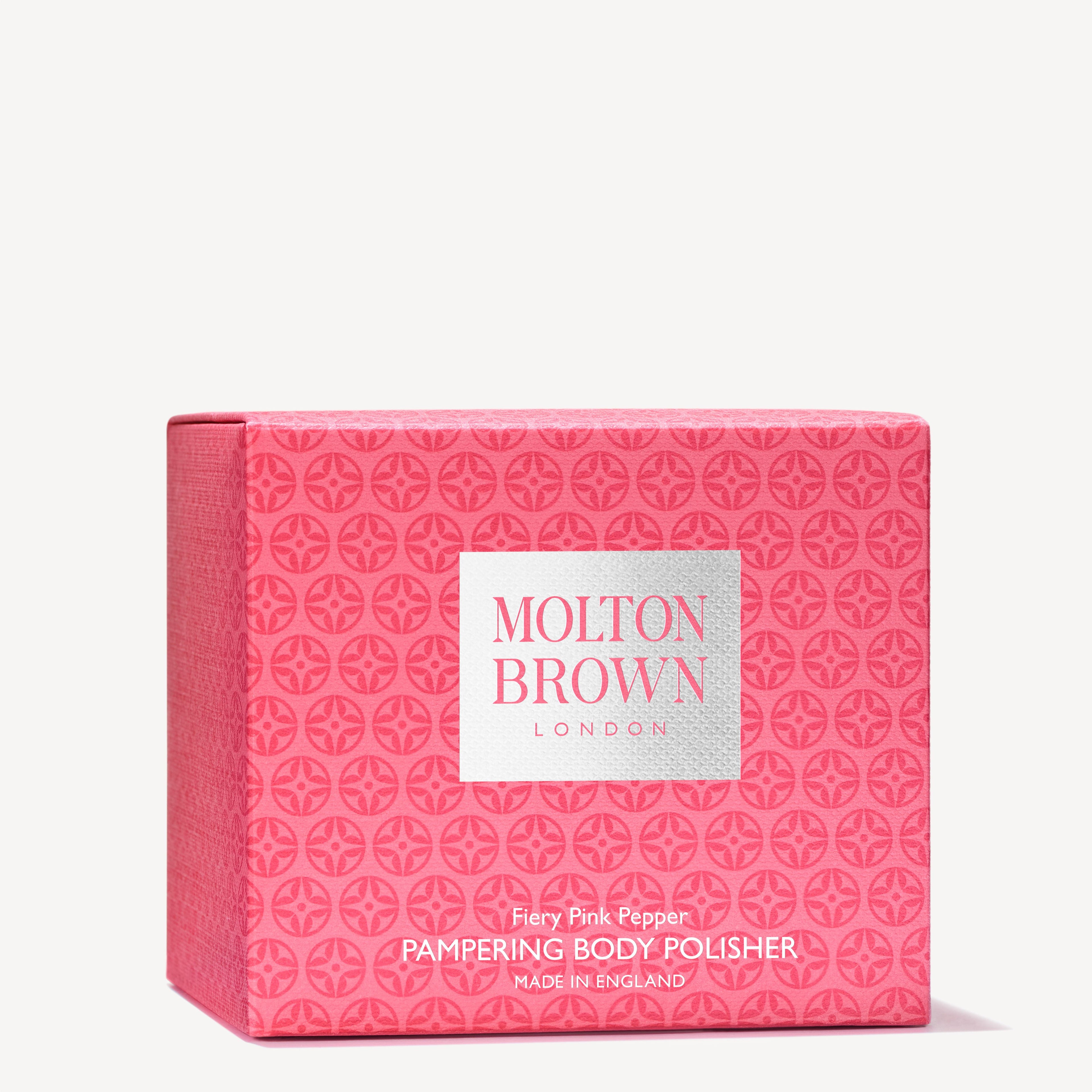 A pink box of MoltonBrown Nederlands Fiery Pink Pepper Pampering Body Polisher 275g, with a repeating circular pattern and white label, enriched with exfoliërende jojoba korrels for a radiant glow.
