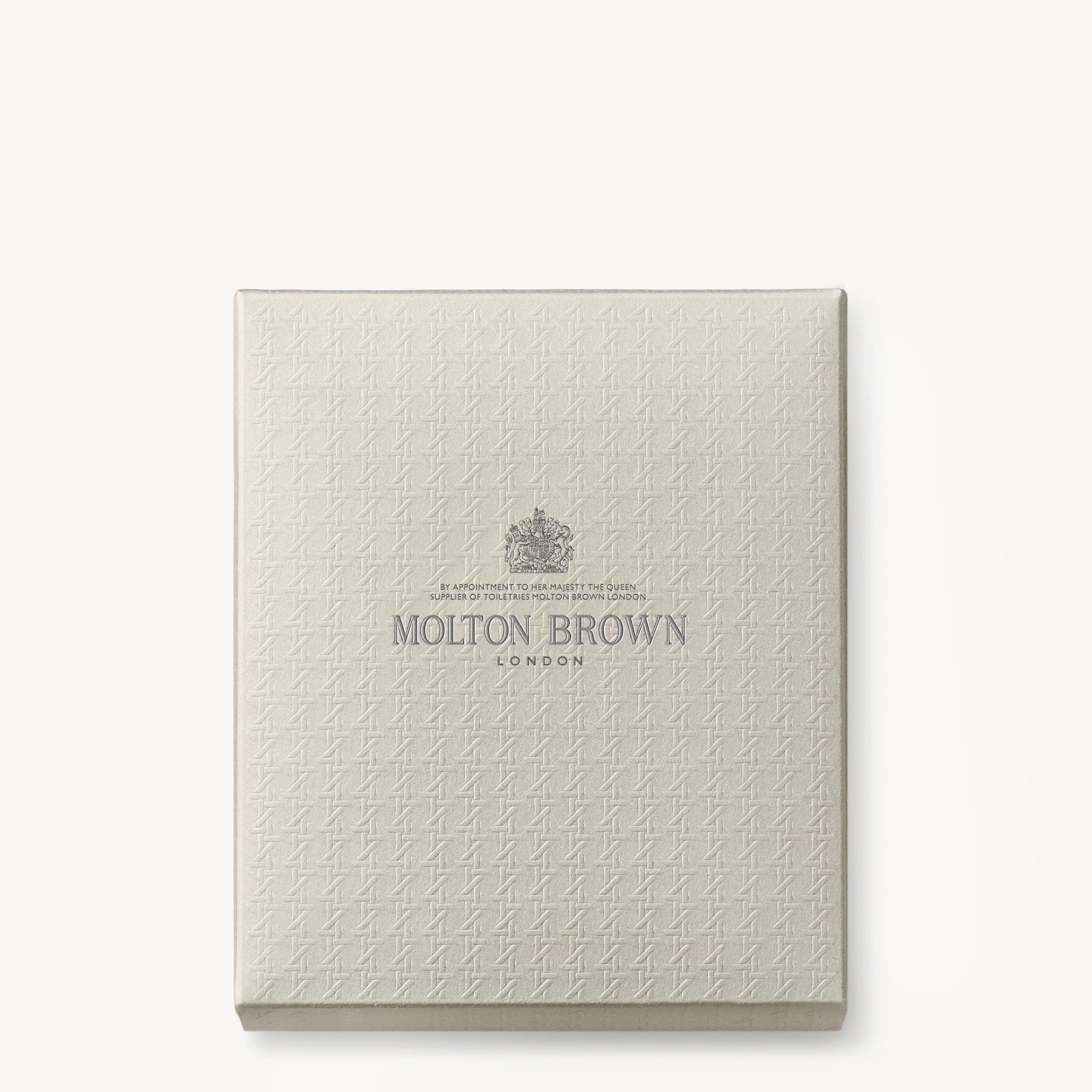 A square, textured, cream-colored Aromatic & Ambery Fragrance Ontdekkingsset gift box from MoltonBrown Nederlands features a subtle pattern and elegant silver lettering centered on the lid.