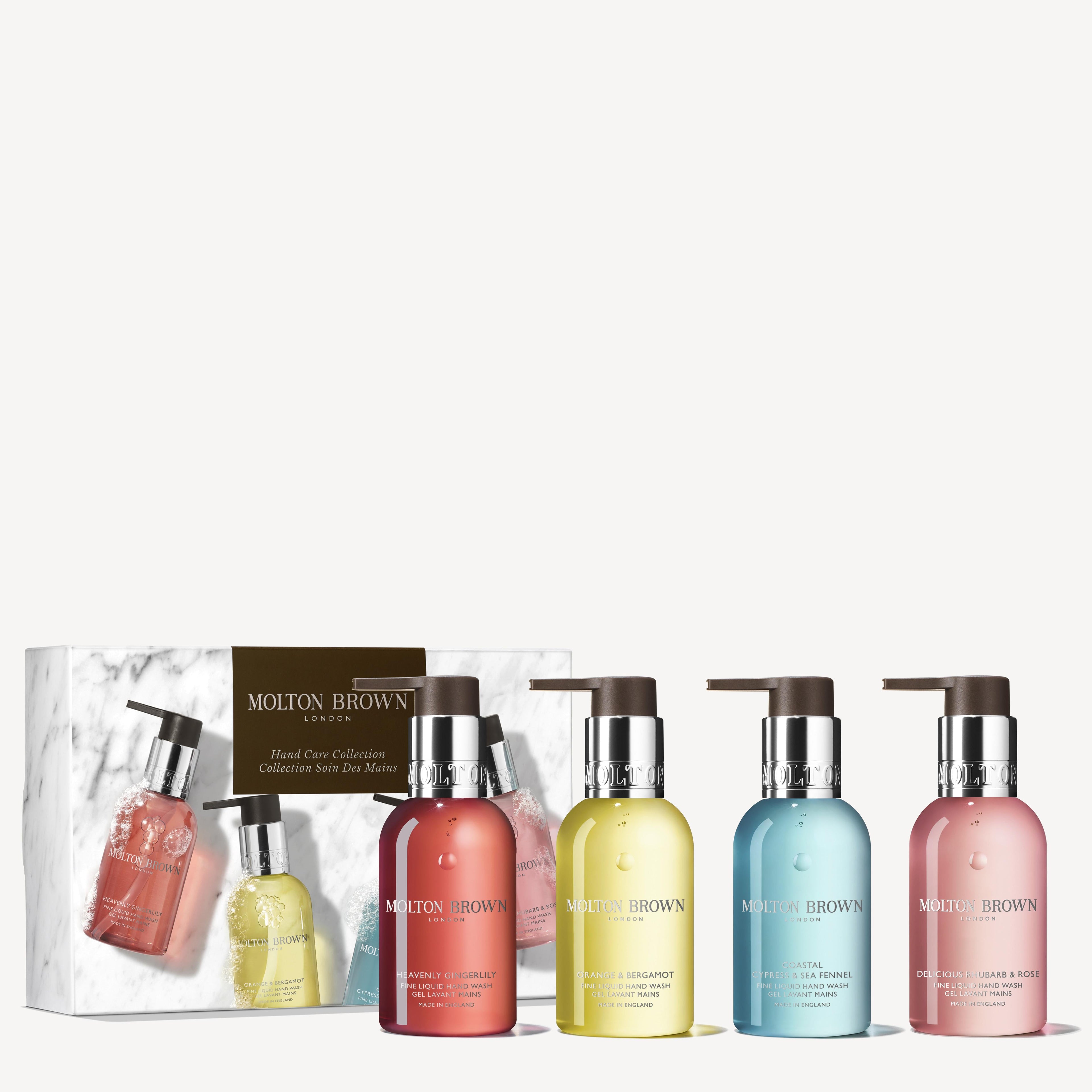 A MoltonBrown Nederlands Fresh & Floral Hand Verzorgingscollectie box is displayed behind four pump bottles in pink, blue, yellow, and orange, each filled with vibrant handzeep in clear, colorful liquid.