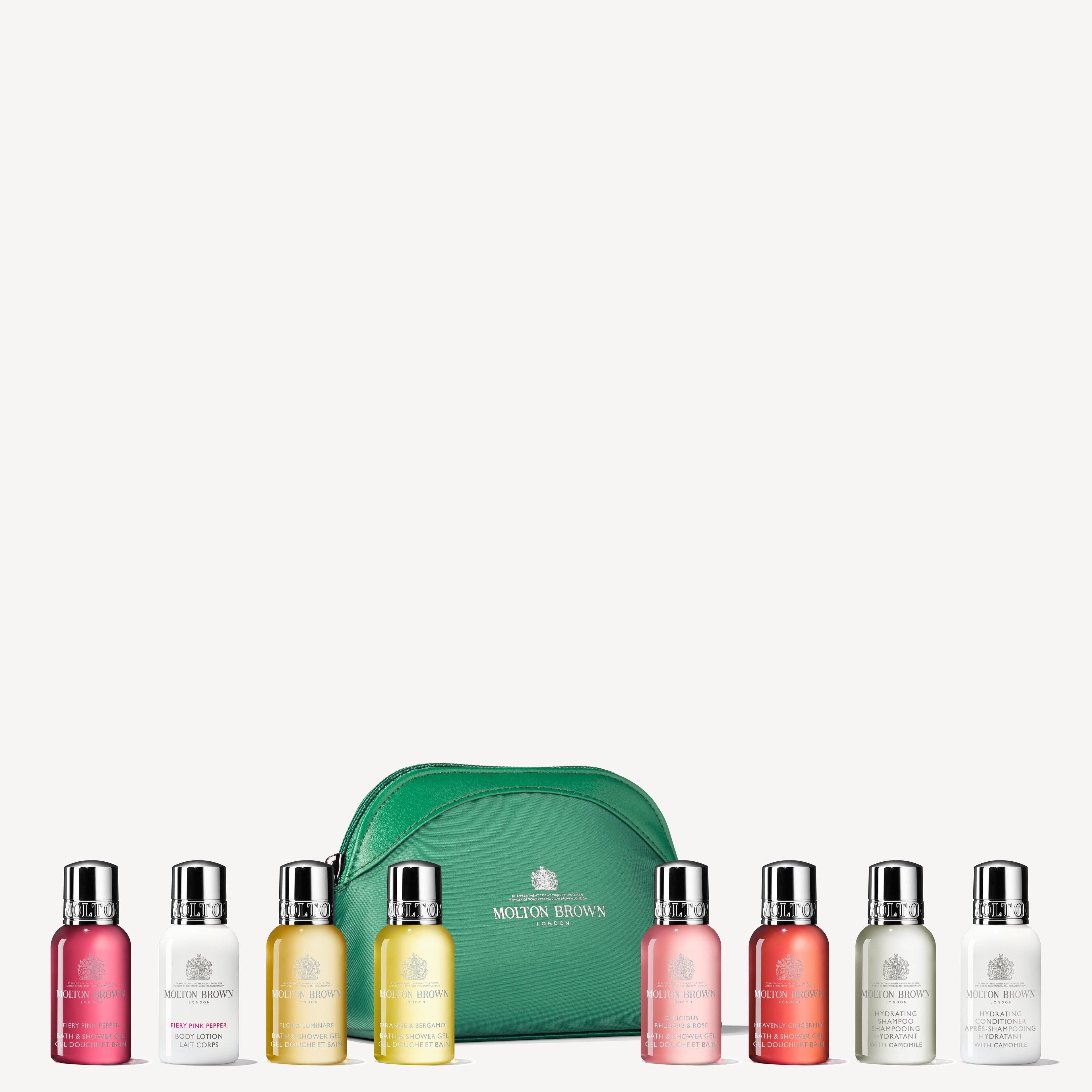 A green The Elegant Escapist Body & Hair Mini Reistas by MoltonBrown Nederlands is displayed with eight reisformaat luxe bath and body bottles in assorted colors, lined up in front of the bag.