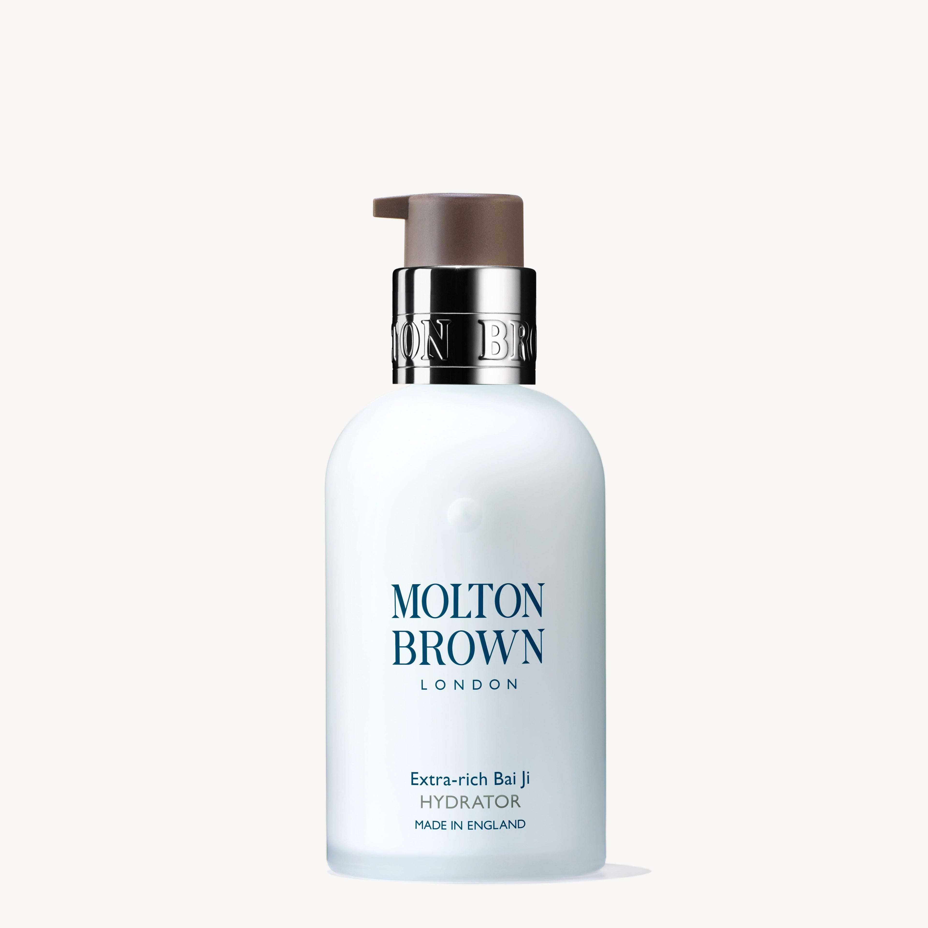 A white 100ml pump bottle of MoltonBrown Nederlands Extra-rich Bai Ji Hydrator, featuring a silver collar and formulated for intense hydration, stands upright against a plain light background.