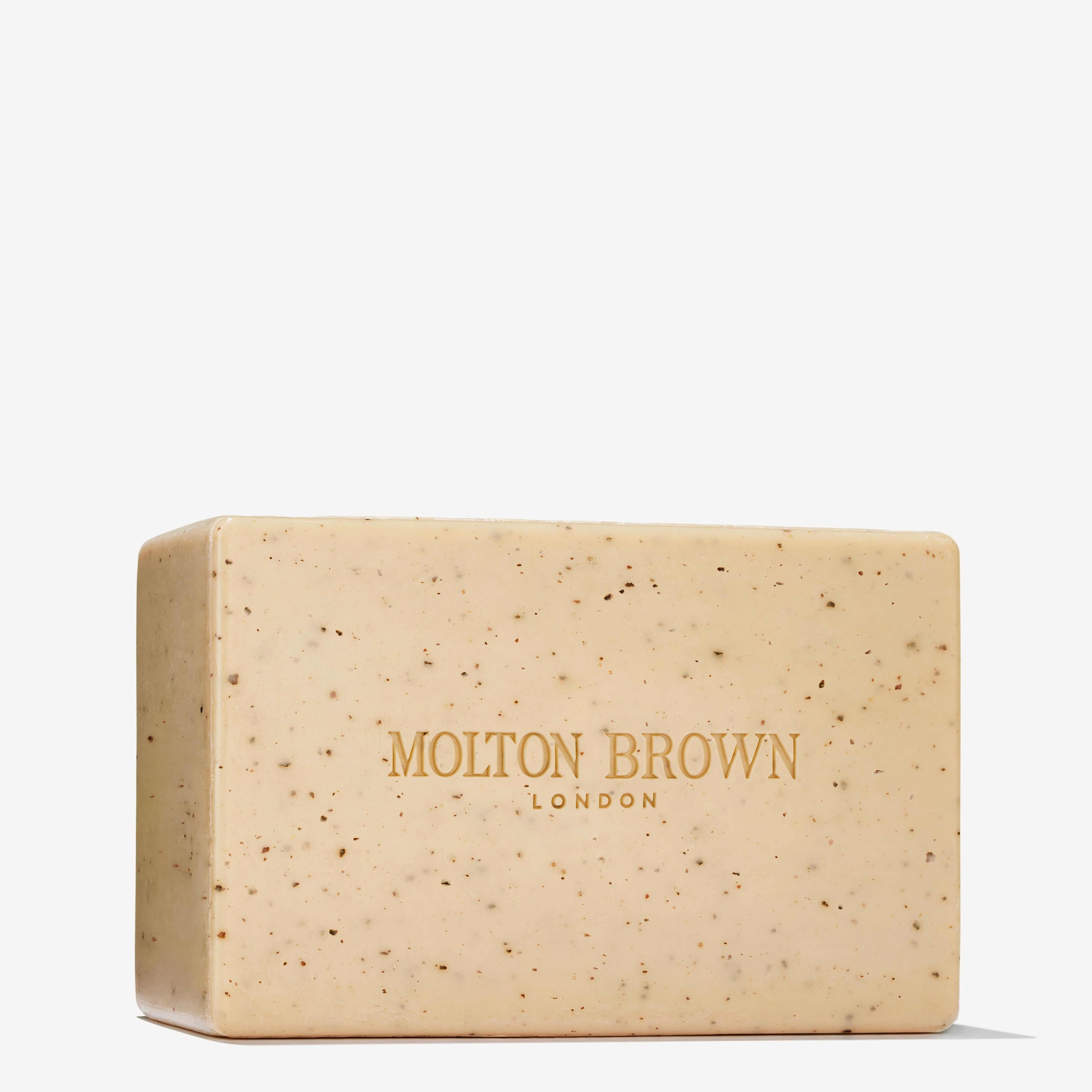 A rectangular beige Re-charge Black Pepper Bodyscrub Bar 250g by MoltonBrown Nederlands, featuring small brown jojoba korrels and gold branding on the front, displayed against a plain white background.