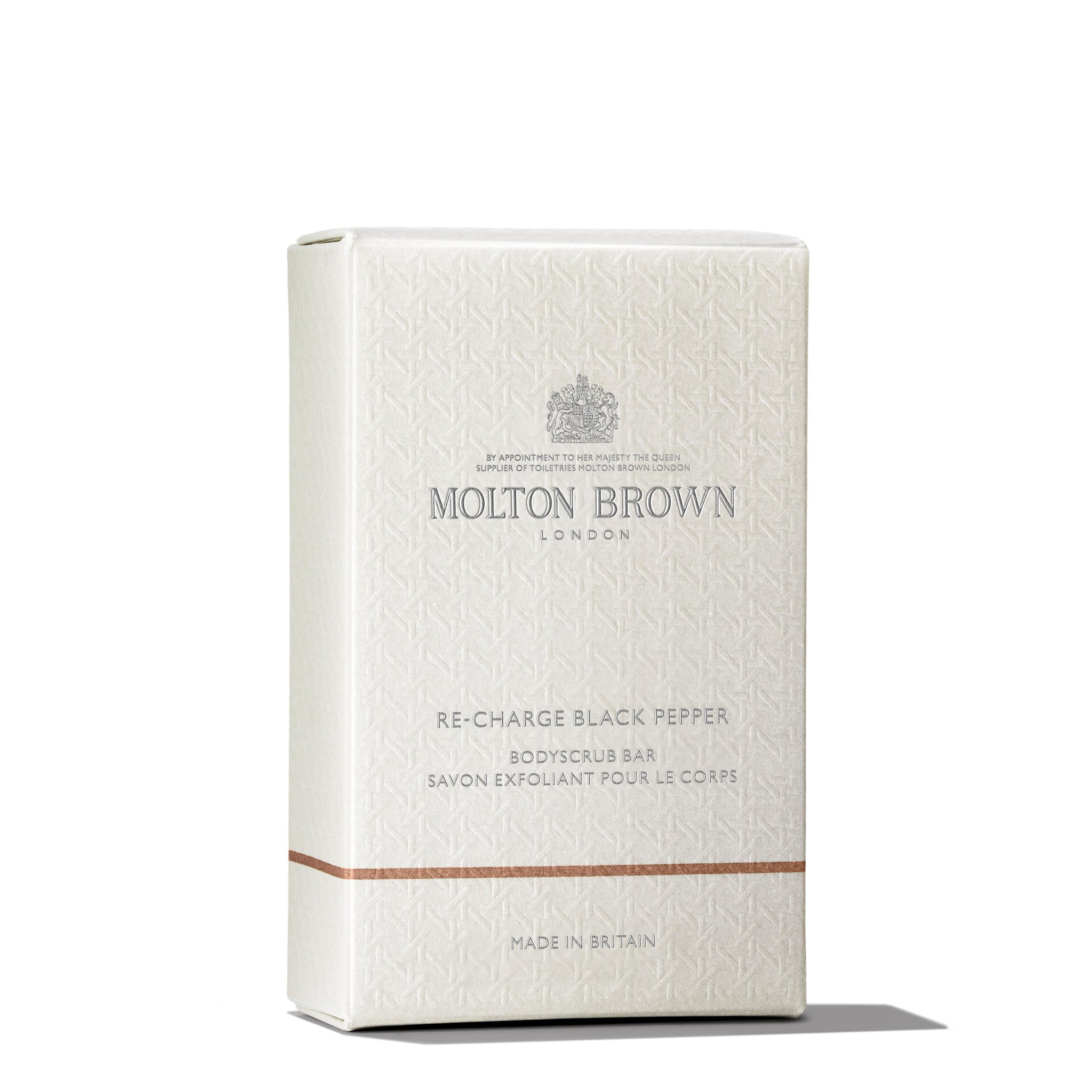 A cream-colored rectangular box of MoltonBrown Nederlands Re-charge Black Pepper Bodyscrub Bar 250g features subtle patterns, silver text, a slim bronze stripe near the base, and is enriched with voedende oliën for an invigorating cleanse.
