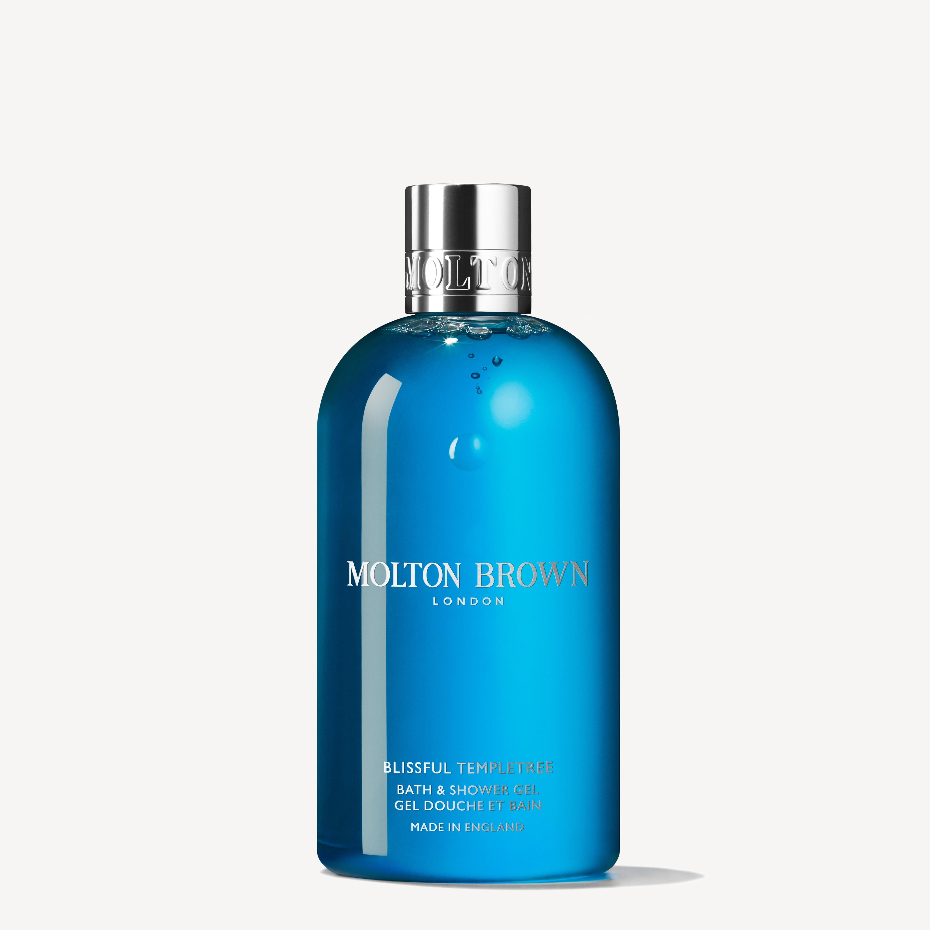 A blue bottle of MoltonBrown Nederlands Blissful Templetree Bad- & Douchegel 300ml with a silver cap, featuring notes of zoete sinaasappel and cederhout, is displayed against a plain white background.