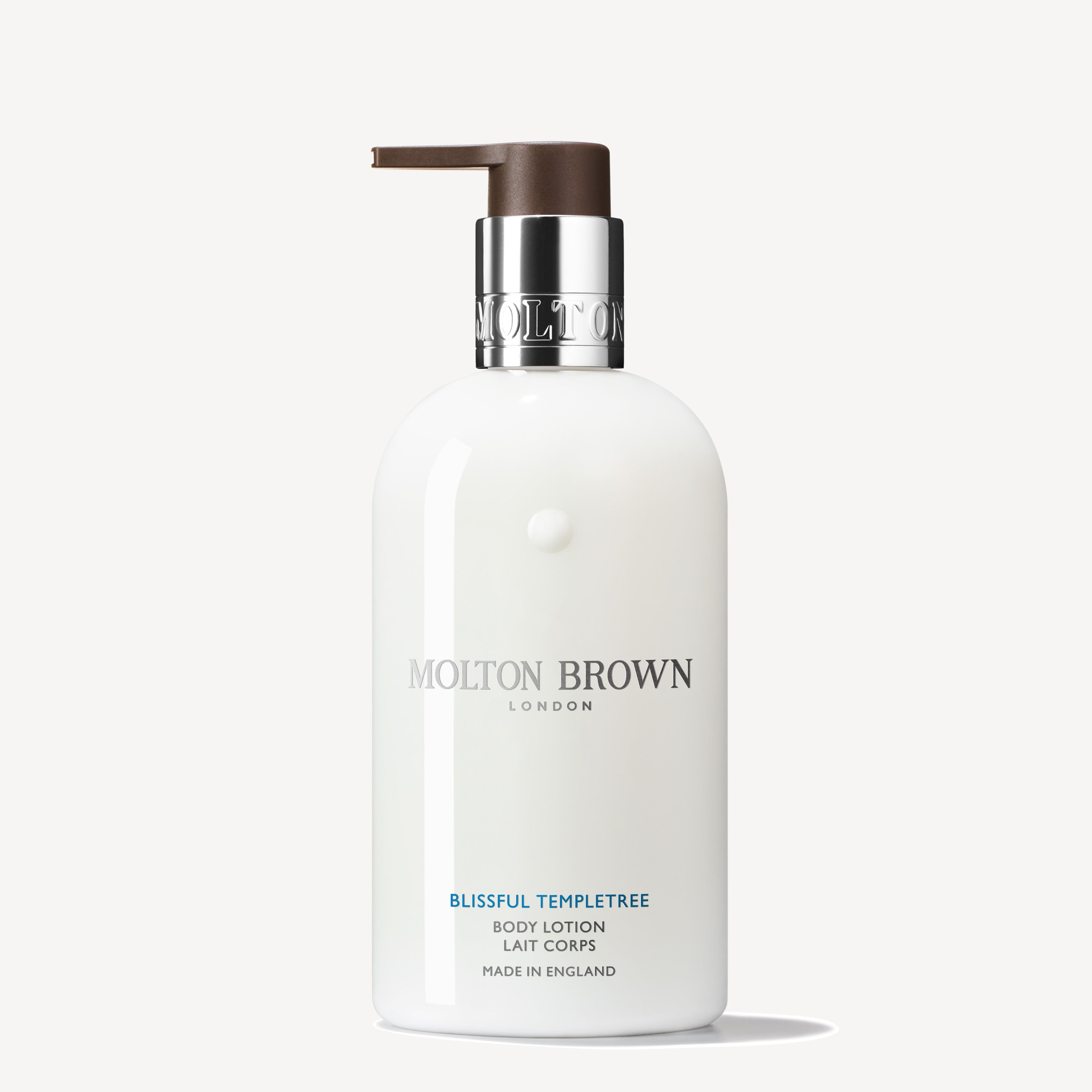 A white bottle of MoltonBrown Nederlands Blissful Templetree Bodylotion 300ml with a silver collar and brown pump sits against a light background; this rich lotion hydrates deeply and has sweet orange notes.