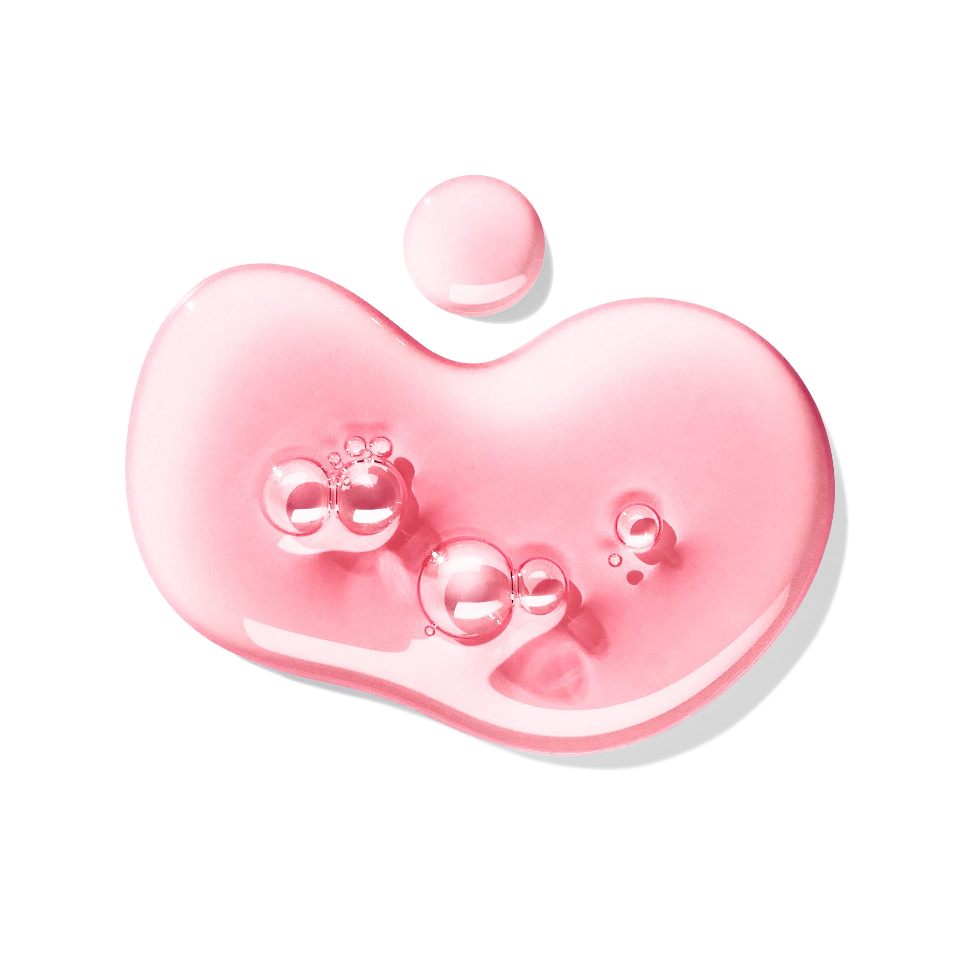An irregular pink liquid drop with bubbles and a smaller drop evoke the fresh scent of MoltonBrown Nederlands Fiery Pink Pepper Bad- & Douchegel 300ml, with roze peper and patchouli, displayed on a white background.