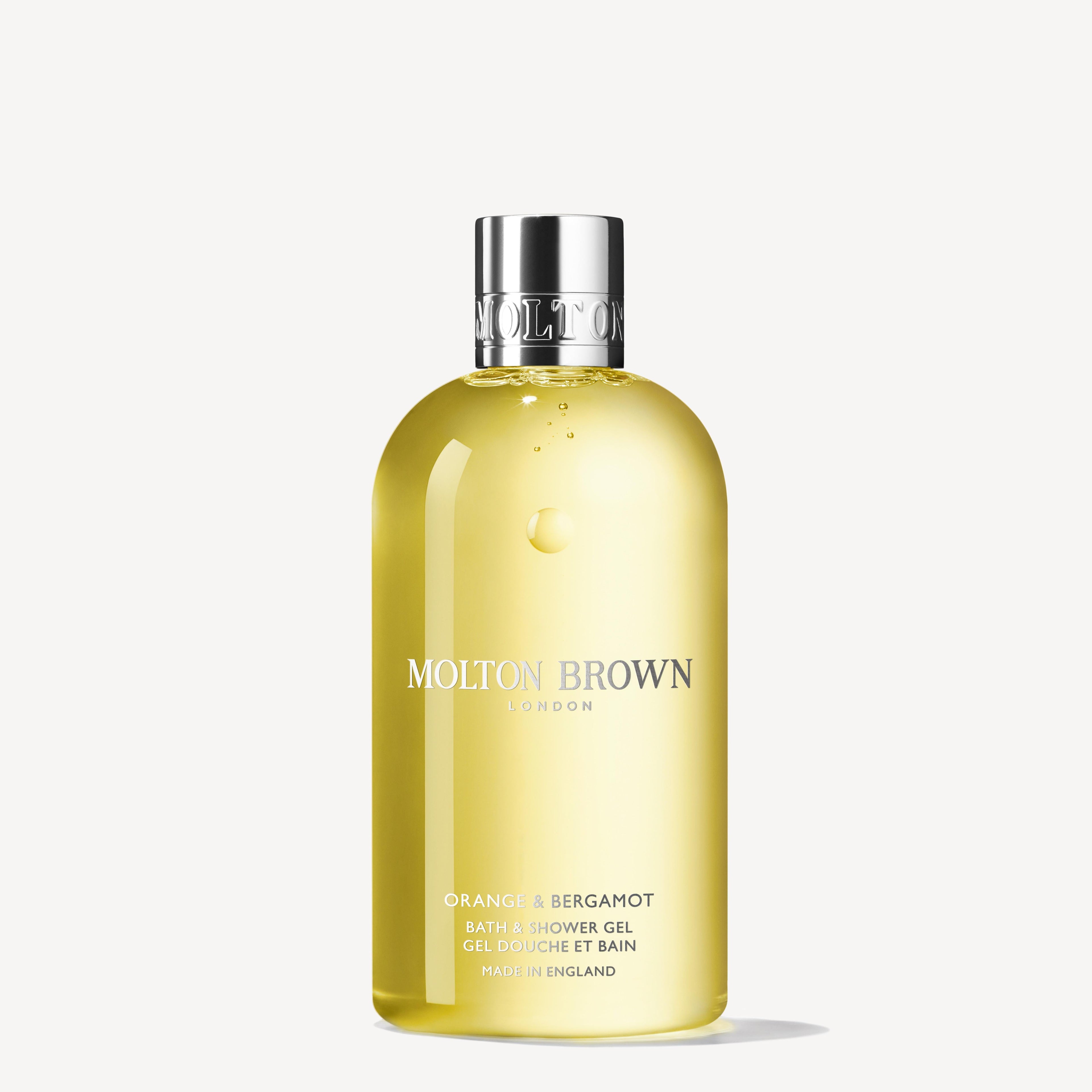 A clear bottle of MoltonBrown Nederlands Orange & Bergamot Bad- & Douchegel 300ml with a silver cap holds yellow, orange and bergamot-scented liquid, displayed against a plain white background.