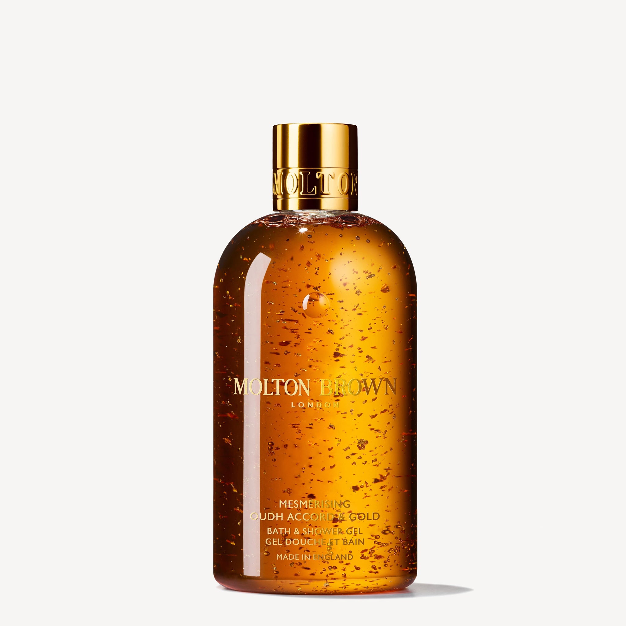 A clear bottle of MoltonBrown Nederlands Mesmerising Oudh Accord & Gold Bad- & Douchegel 300ml, with echte oudh and gold flecks, topped with a shiny cap, exudes a luxurious scent against a white background.