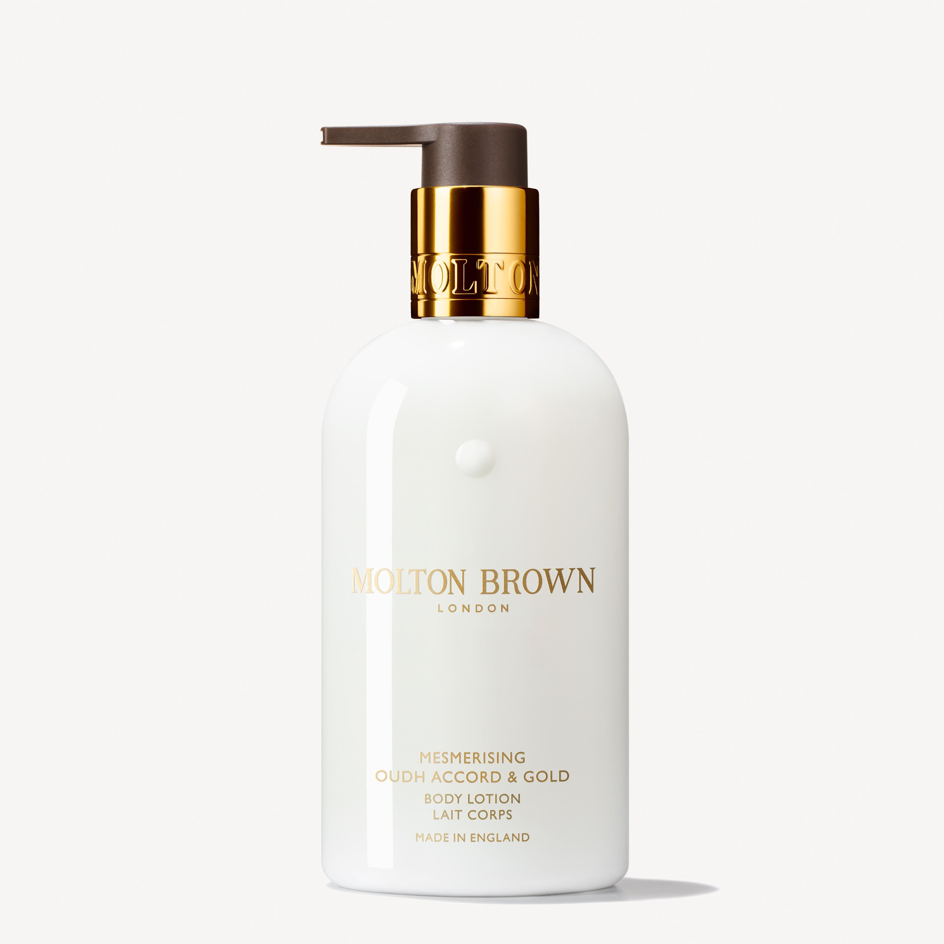 A white 300ml bottle of MoltonBrown Nederlands Mesmerising Oudh Accord & Gold Bodylotion with a gold and brown pump stands upright against a plain white background.