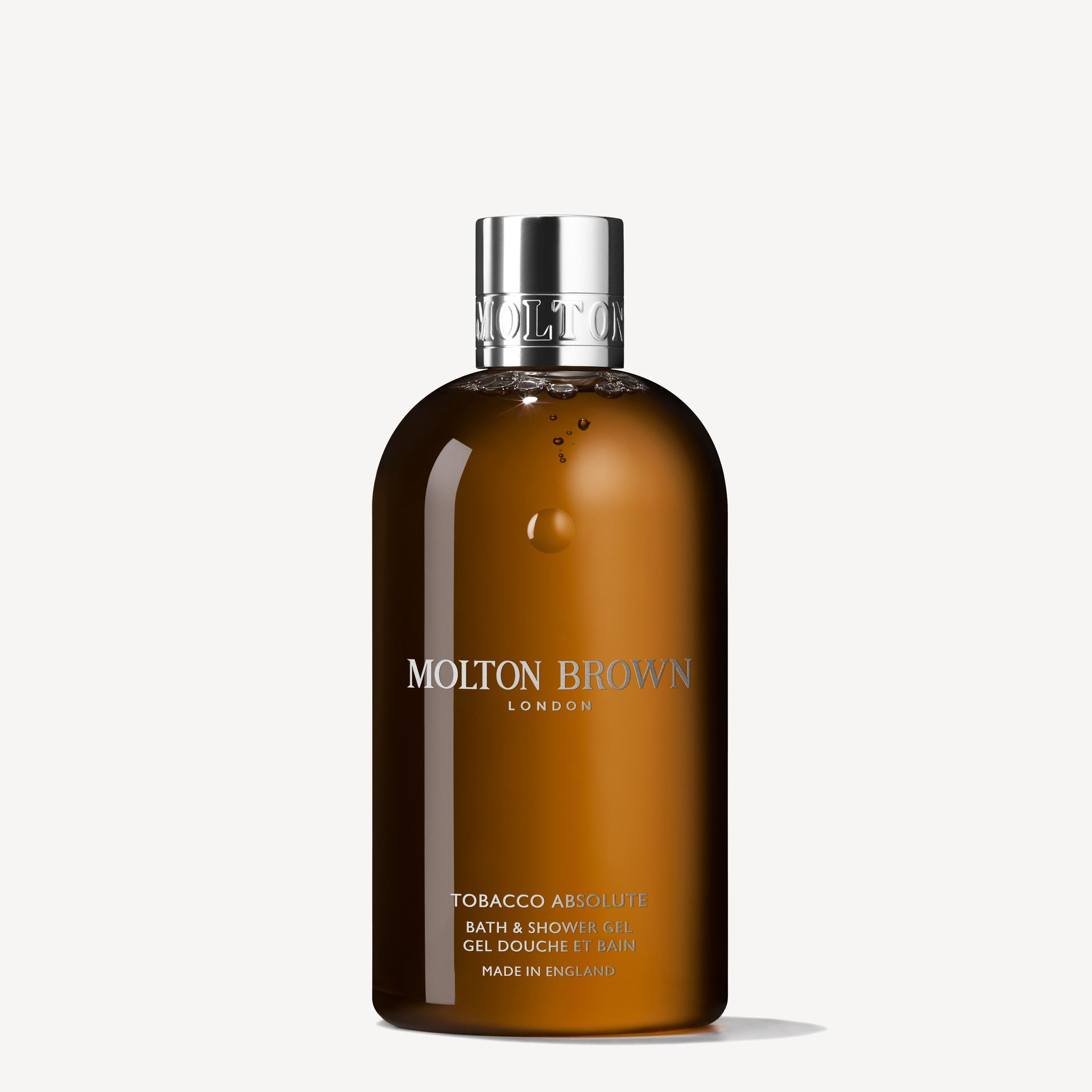 A brown bottle of MoltonBrown Nederlands Tobacco Absolute Bad- & Douchegel 300ml with a silver cap, featuring white and gold labeling, stands upright on a white background—een elegante houtige douchegel met accenten van tabaksblad.