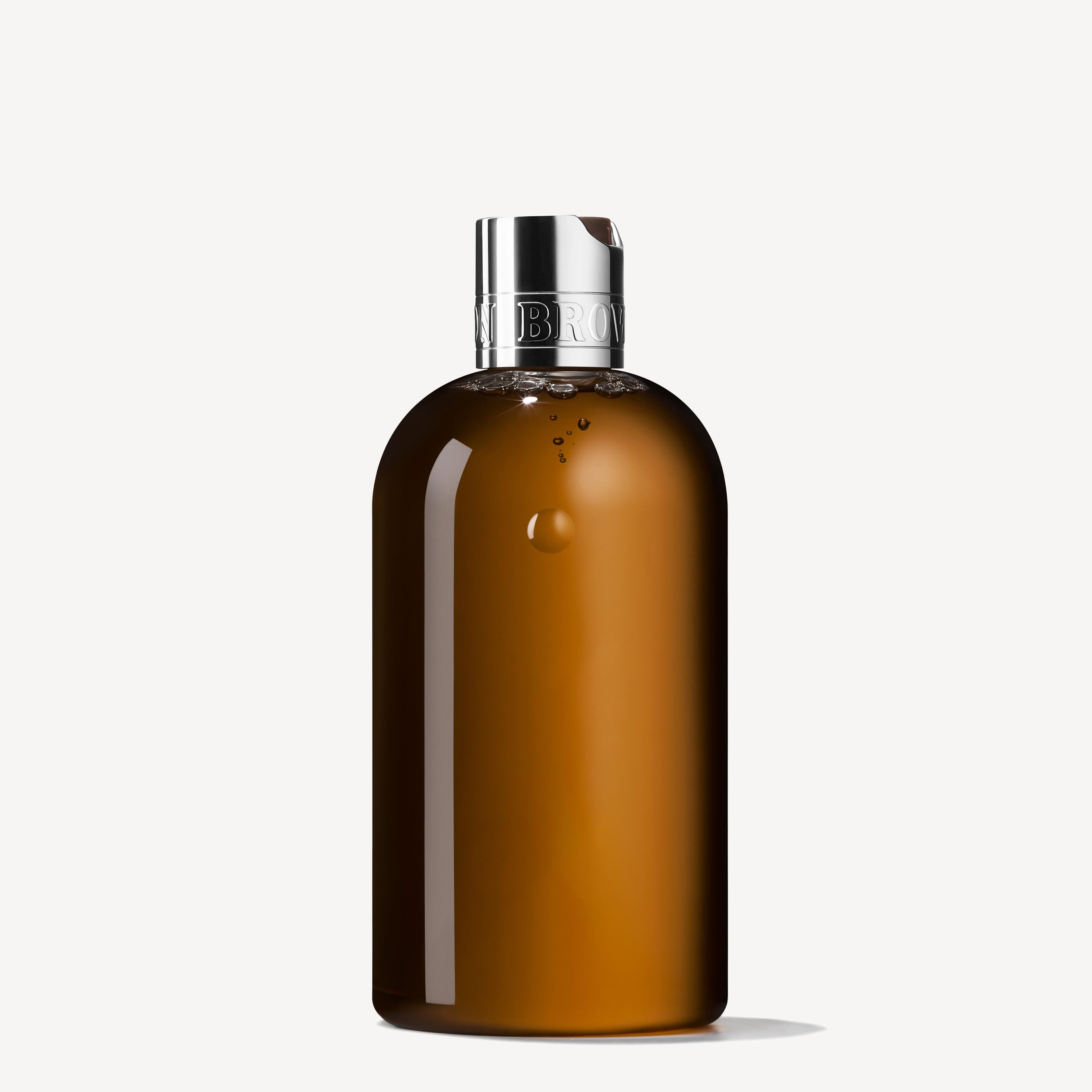 A brown translucent bottle with a shiny silver cap and metallic band, MoltonBrown Nederlands Tobacco Absolute Bad- & Douchegel 300ml features a minimalist, unlabelled design that evokes luxe houtige and tabaksblad against a plain white background.