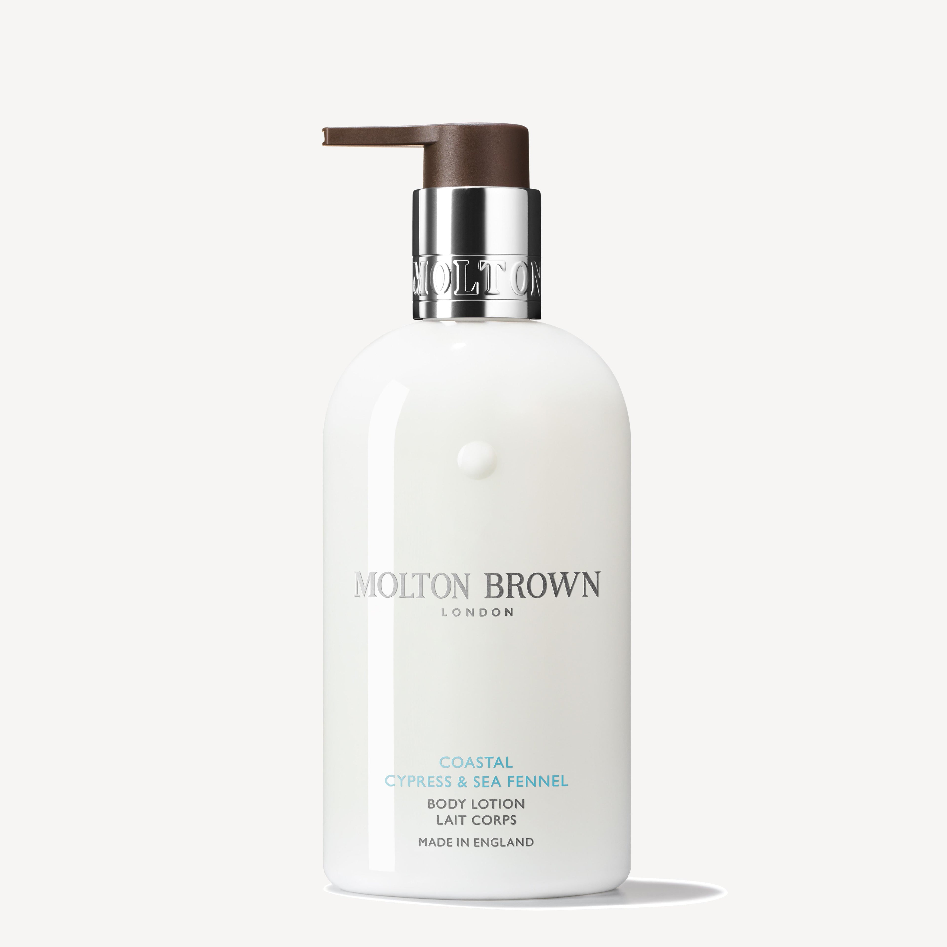 Een witte MoltonBrown Nederlands Coastal Cypress & Sea Fennel Bodylotion 300ml fles met bruine pomp, zilveren en lichtblauwe tekst. Hydraterende formule met frisse zee-ontmoet-land geur, Made in England.