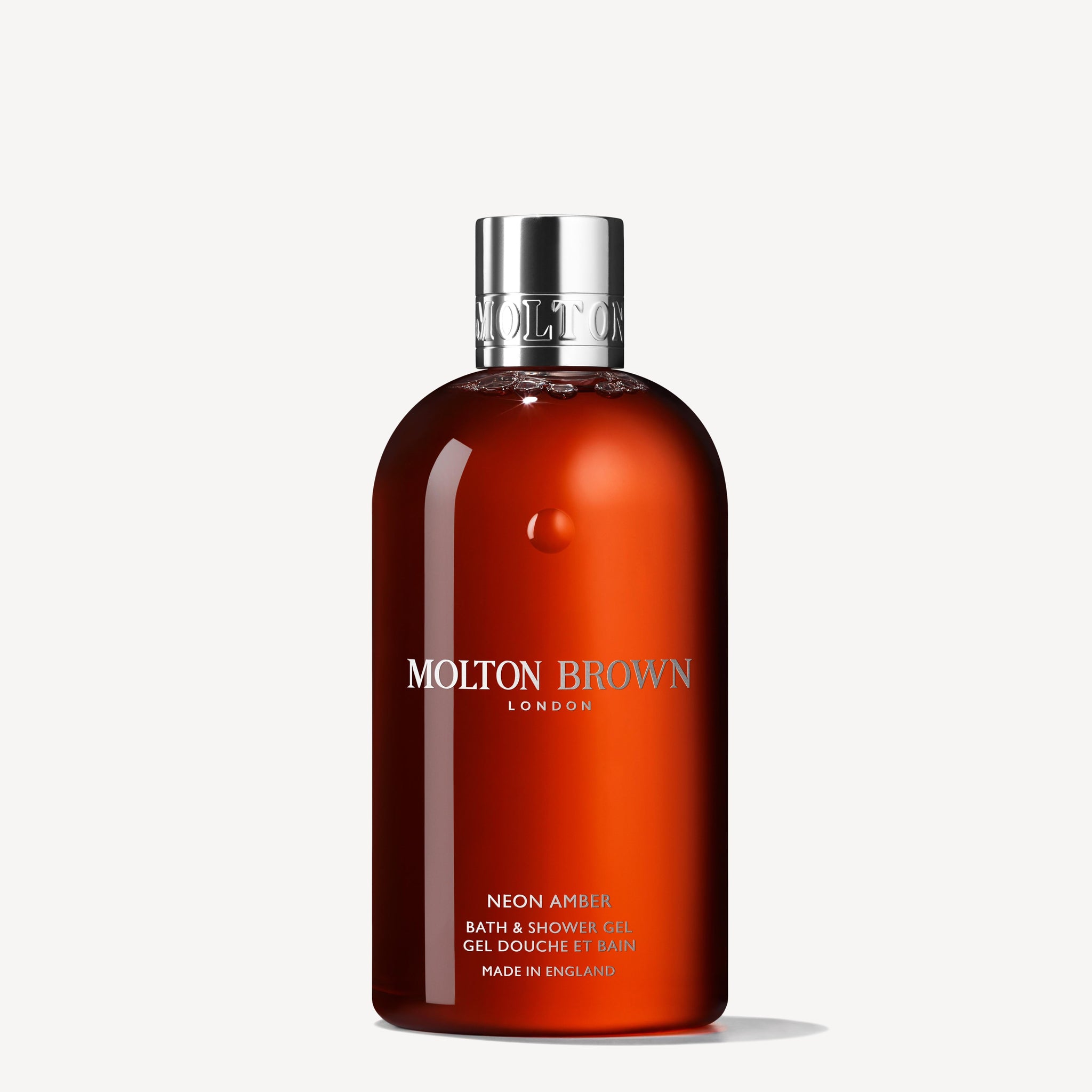 A 300ml bottle of MoltonBrown Nederlands Neon Amber Bad- & Douchegel features a shiny silver cap and orange-tinted translucent body, displayed against a plain white background.
