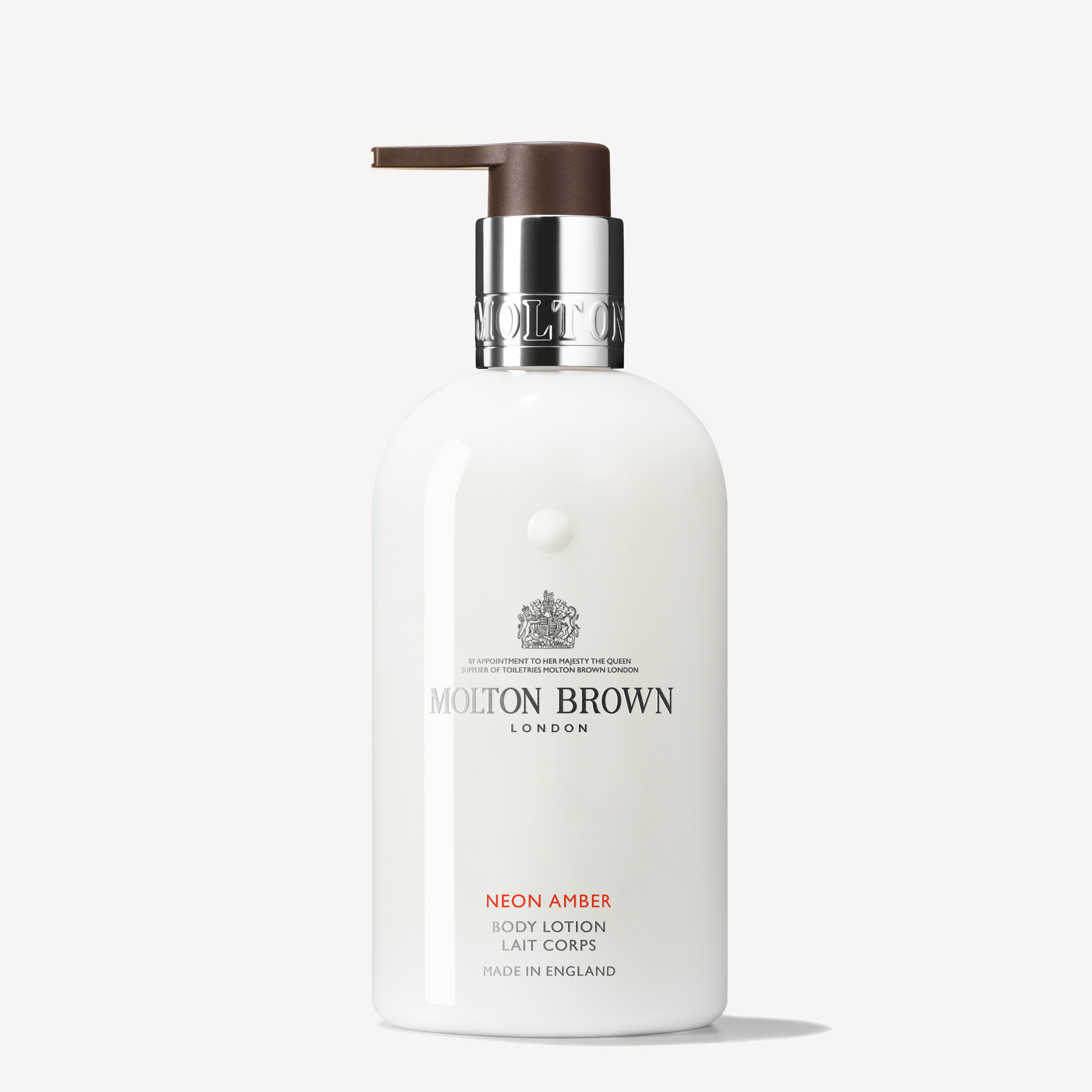 A white 300ml bottle of MoltonBrown Nederlands Neon Amber Bodylotion with a silver collar and dark brown pump, set against a plain white background. The amberachtige formule helpt de huid hydrateren.