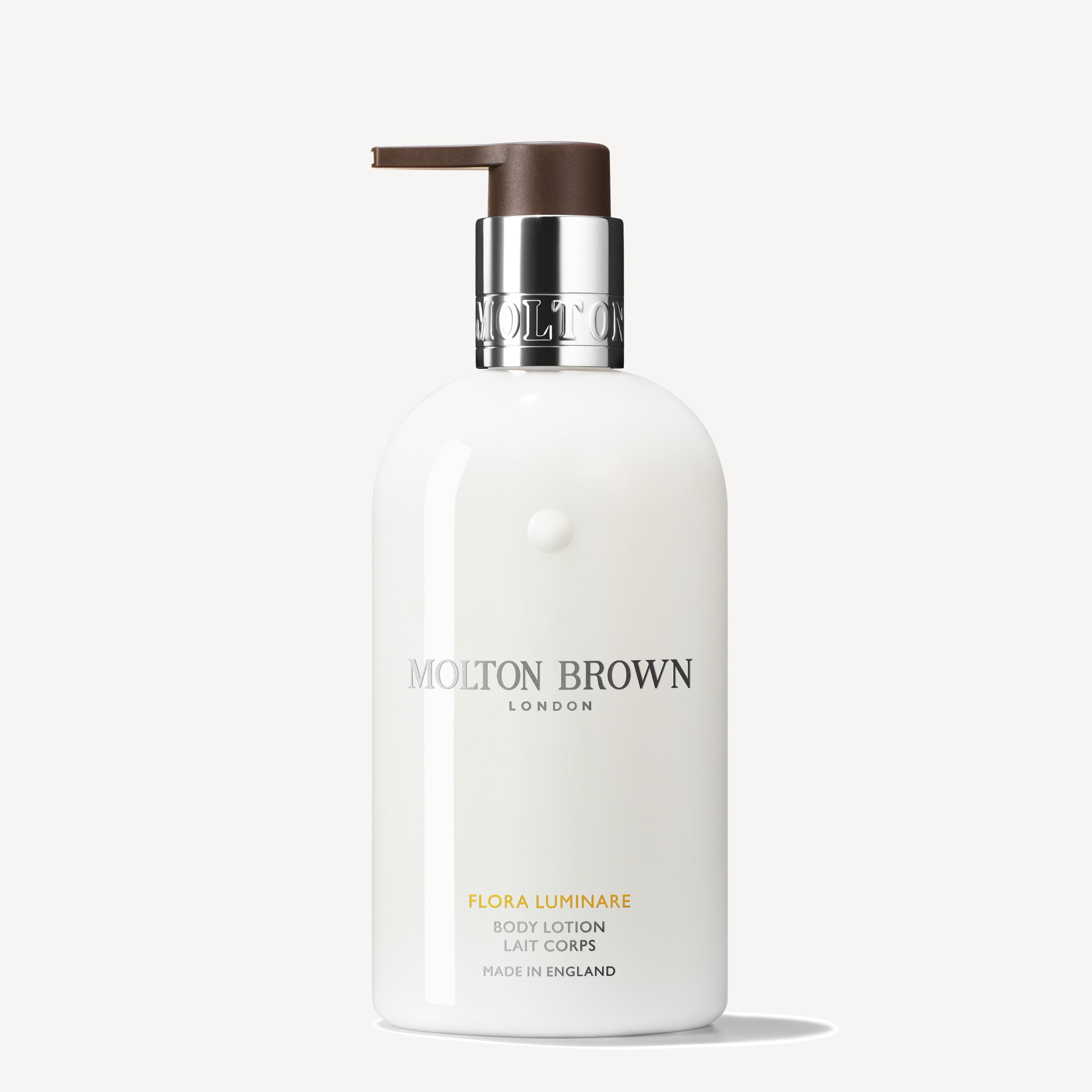 A white 300ml MoltonBrown Nederlands Flora Luminare Bodylotion with a silver collar and brown pump, minimalist text, and delicate tiaré and sinaasappelbloesem notes.