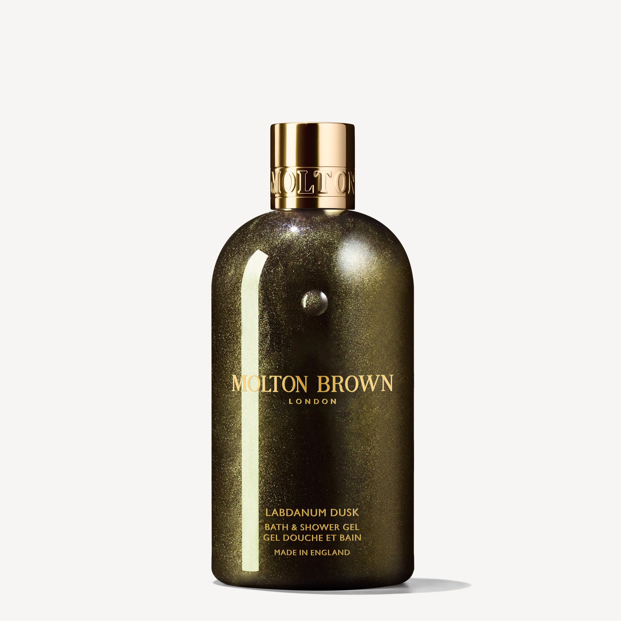 A shimmering dark green 300ml bottle of MoltonBrown Nederlands Labdanum Dusk Bad- & Douchegel with a gold cap and gold label text stands upright against a plain white background, accented with saffron notes.