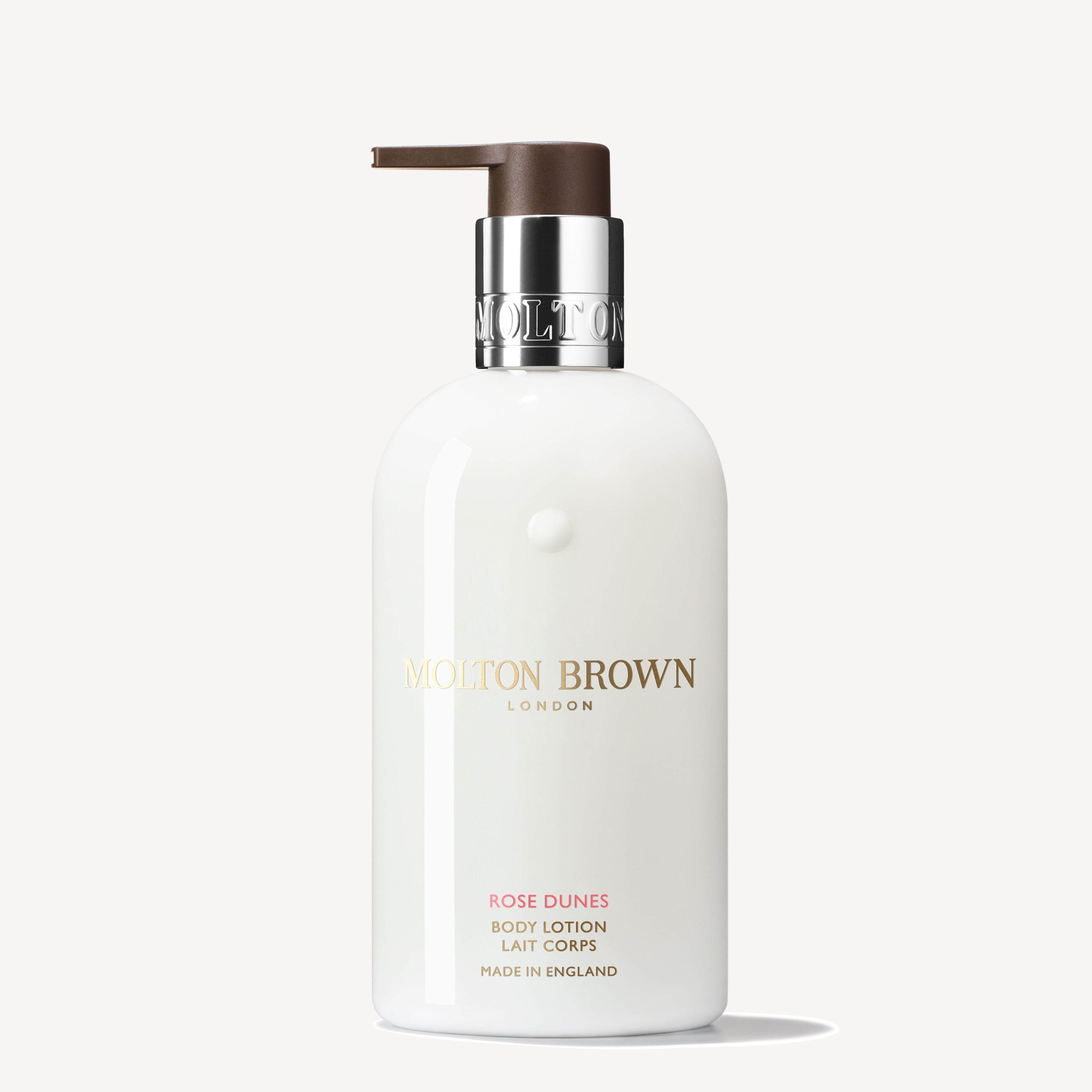 A white bottle of MoltonBrown Nederlands Rose Dunes Bodylotion 300ml with a brown pump and silver collar, gold and pink text, blends oudh and Bulgaarse roos; shown against a plain light background.