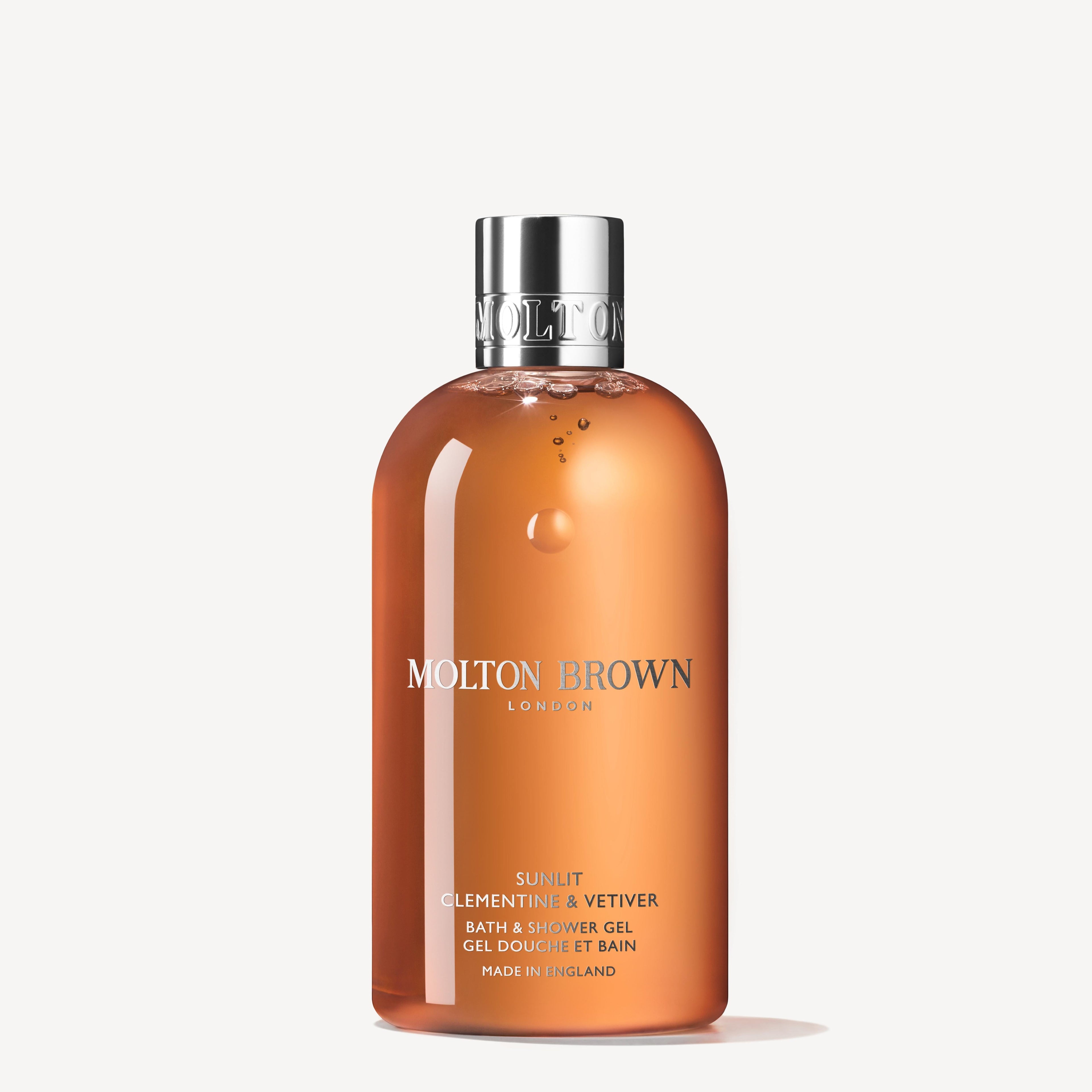A clear 300ml bottle of MoltonBrown Nederlands Sunlit Clementine & Vetiver Bad- & Douchegel, filled with vibrant orange gel, features a silver cap and crisp white label text against a plain white background.
