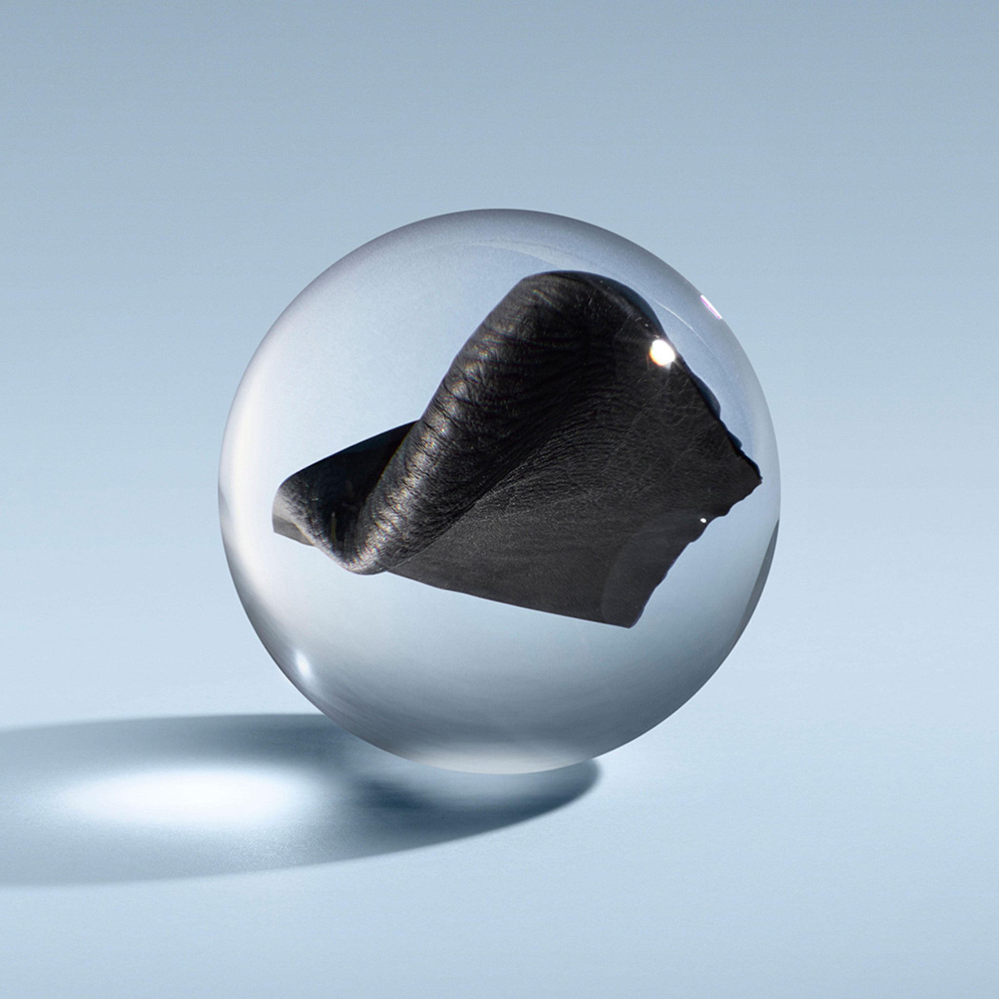 A clear glass sphere with dark leather inside hovers over a smooth blue surface, capturing the spirit of MoltonBrown Nederlands Dark Leather Bad- & Douchegel 300ml and its krachtige, mannelijke geur.
