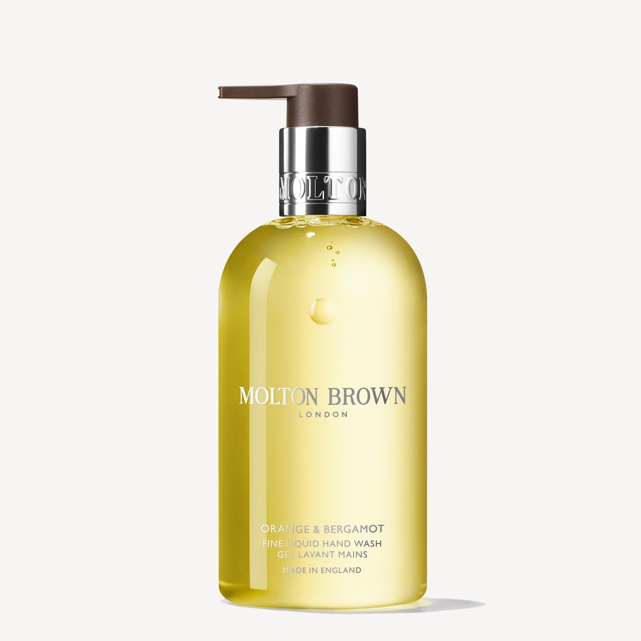 A clear bottle of MoltonBrown Nederlands Orange & Bergamot Vloeibare Handzeep 300ml with a pump dispenser, filled with yellow liquid. White and silver label text. The bottle is set against a plain white background.