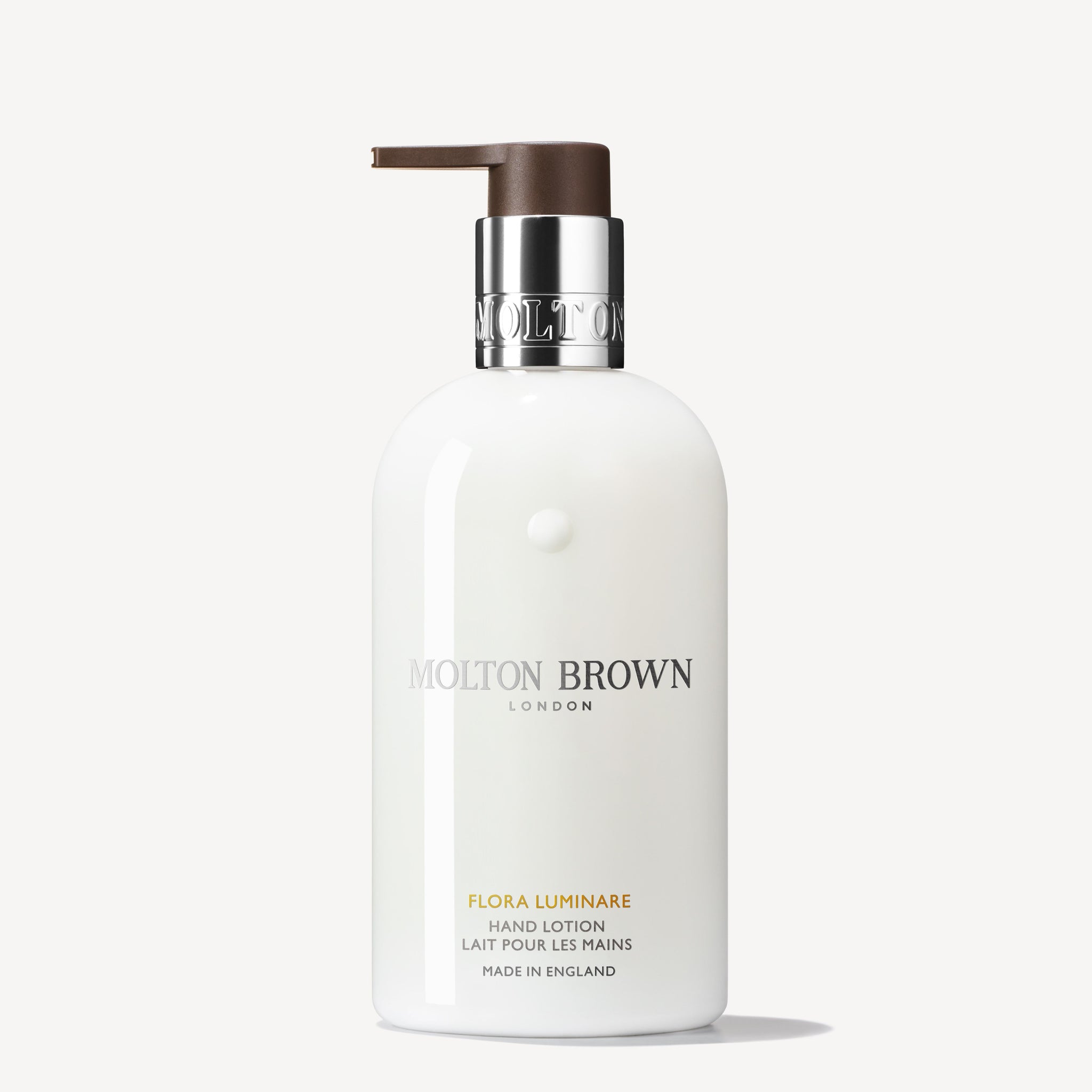 A 300ml white bottle of MoltonBrown Nederlands Flora Luminare Handlotion with a silver collar and brown pump, English and French text, on a plain white background. Verrijkt met hydraterende sinaasappelbloesem.