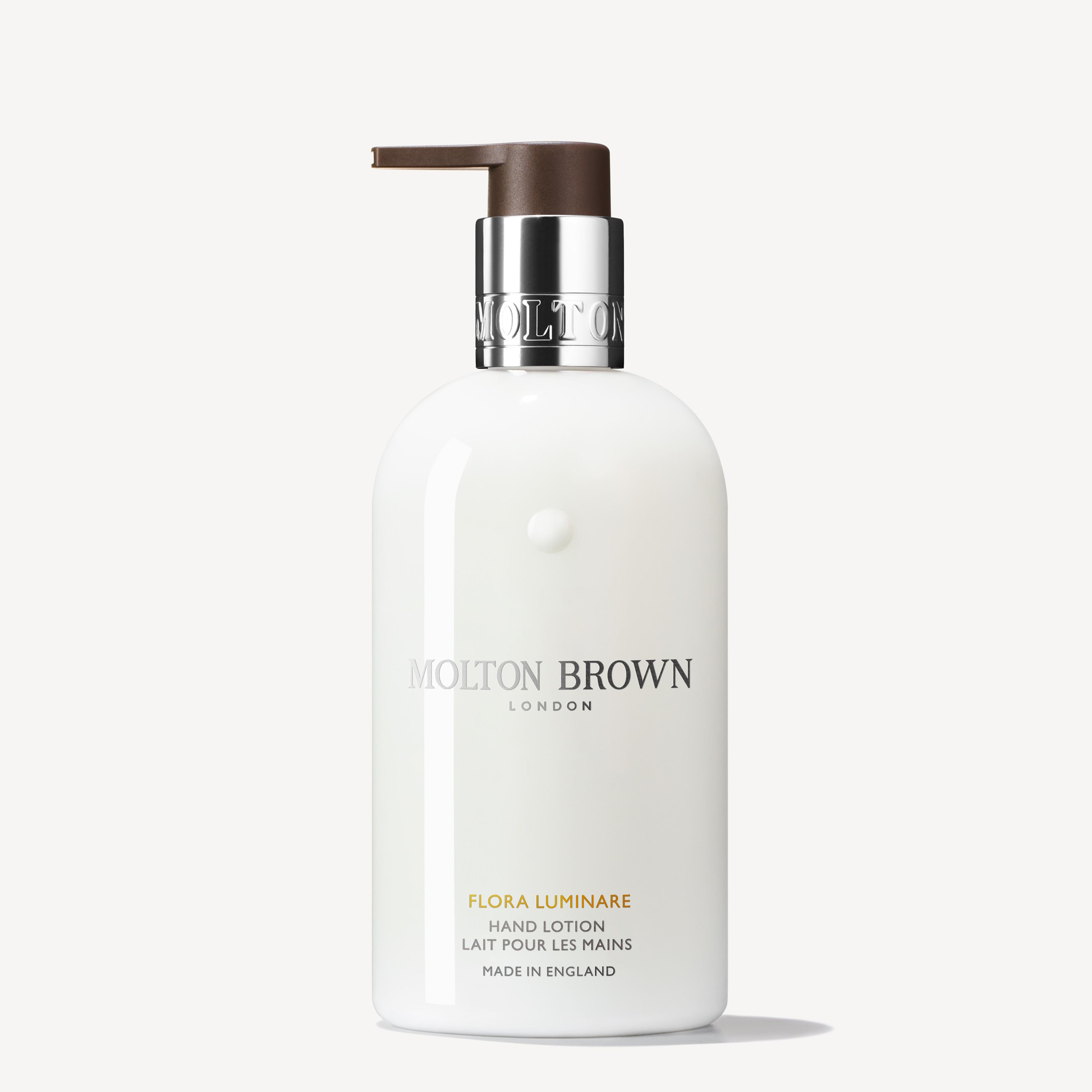 A 300ml white bottle of MoltonBrown Nederlands Flora Luminare Handlotion with a silver collar and brown pump, English and French text, on a plain white background. Verrijkt met hydraterende sinaasappelbloesem.
