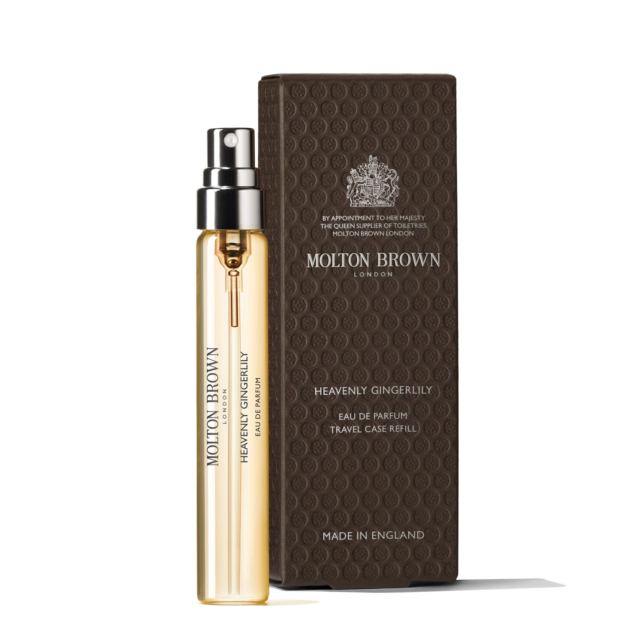 A MoltonBrown Nederlands Heavenly Gingerlily Eau de Parfum Reiskoffer Navulling 7.5ml spray staat naast zijn luxe donkerbruine verpakking met goudaccenten en elegante branding, met een vleugje jasmijn geïnspireerd door witte moerbei-extract.