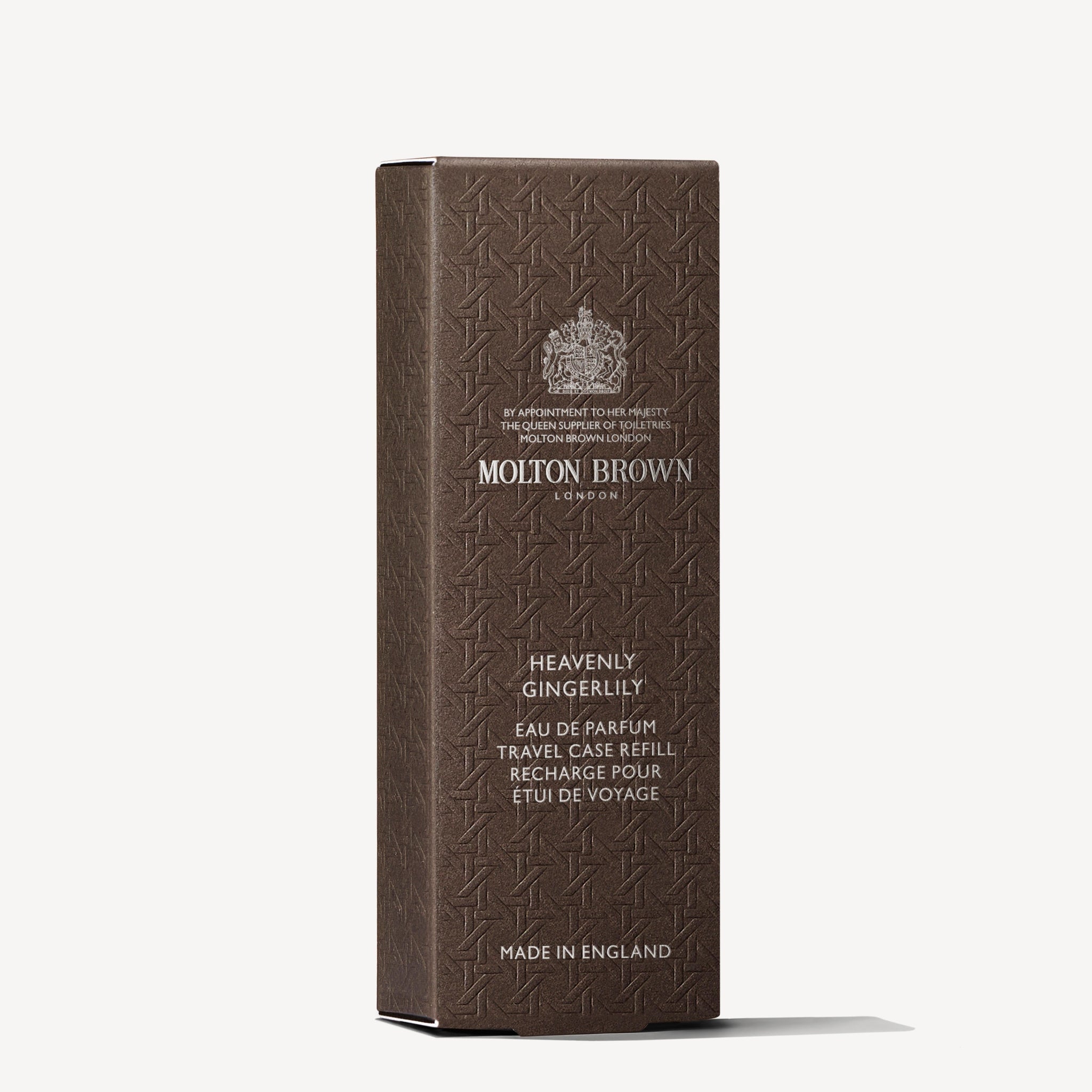 A brown rectangular box of MoltonBrown Nederlands Heavenly Gingerlily Eau de Parfum Reiskoffer Navulling 7.5ml with embossed patterns and silver text stands upright against a white background, inspired by delicate jasmijn scent.