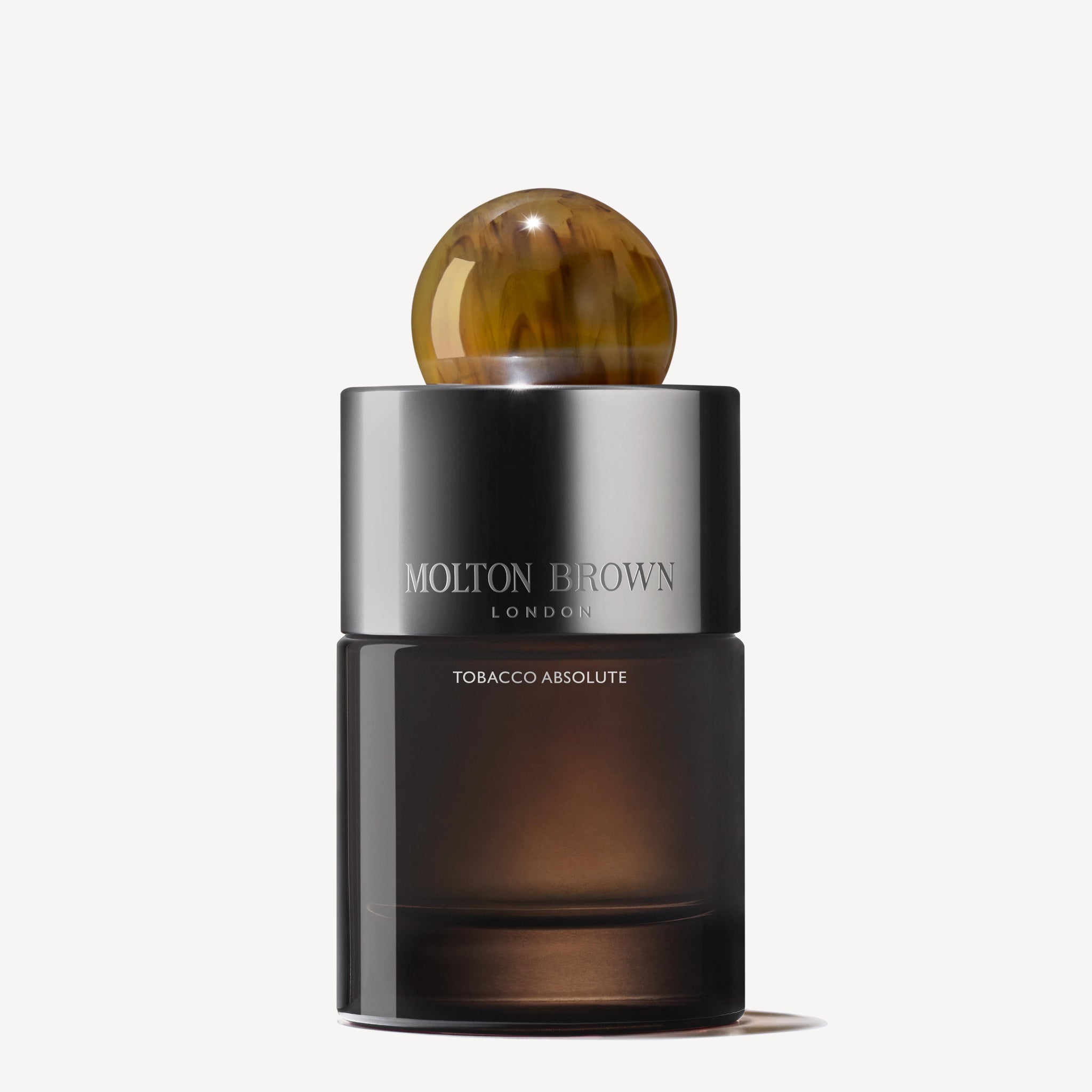 A 100ml MoltonBrown Nederlands Tobacco Absolute Eau de Parfum bottle with a sleek dark glass body, shiny silver band, and round marbled brown cap.